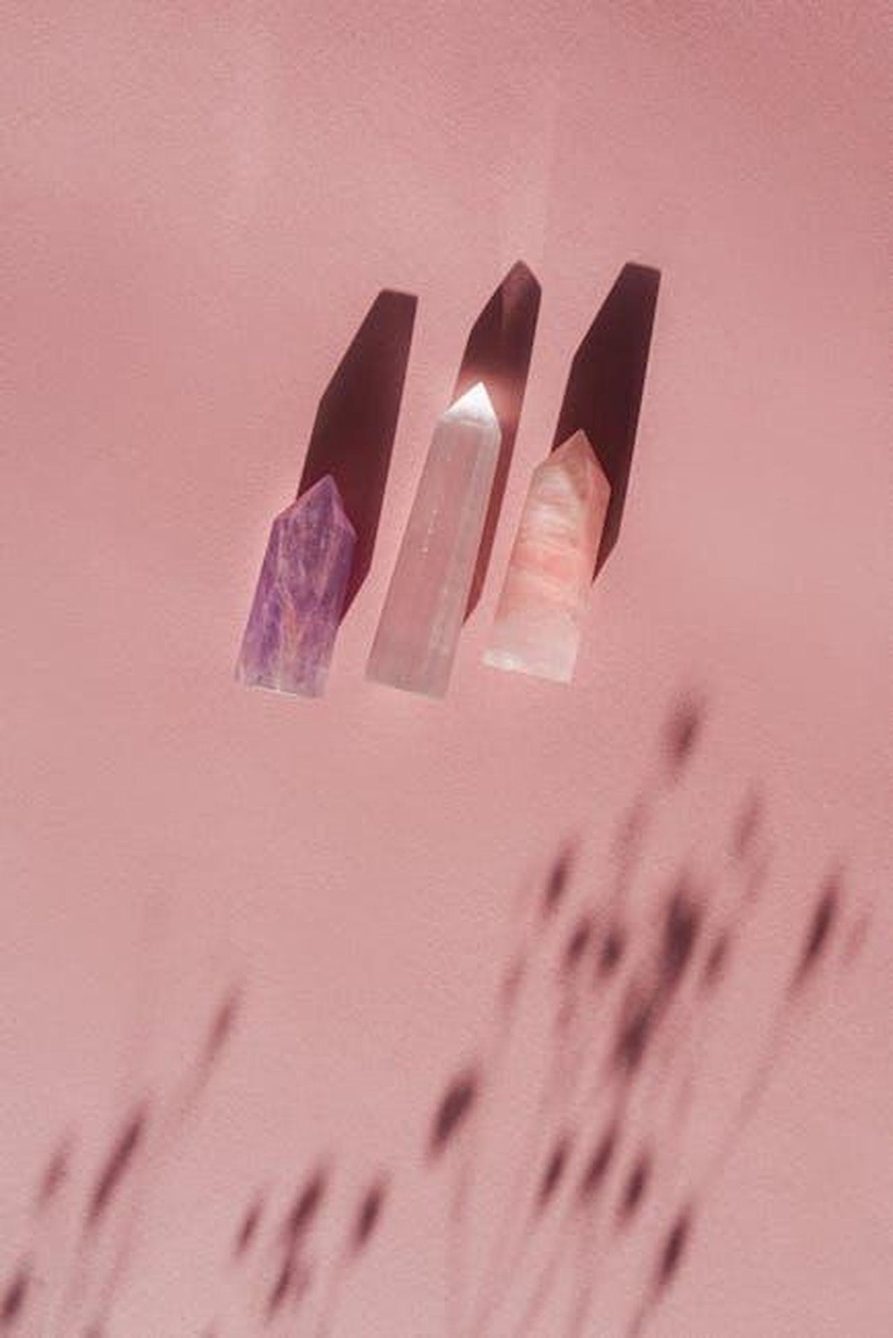 Alternative_e_altre_fragranze_di_Pharmacia_R8IdbNWY4j - Confidenze24 Source: Mikhail Nilov - pexels - Three polished crystals casting shadows on a soft pink surface, creating a tranquil and mystical feel.