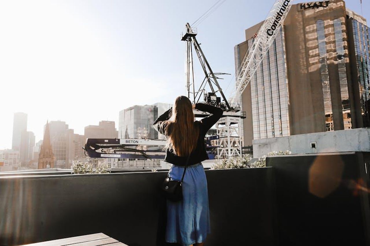 Annuncio_della_Espansione_di_Blue_Bloods_YhoOEigZJD - Confidenze24 Source: Rachel Claire - pexels - A woman stands on a rooftop, observing a construction crane against an urban skyline during sunrise.
