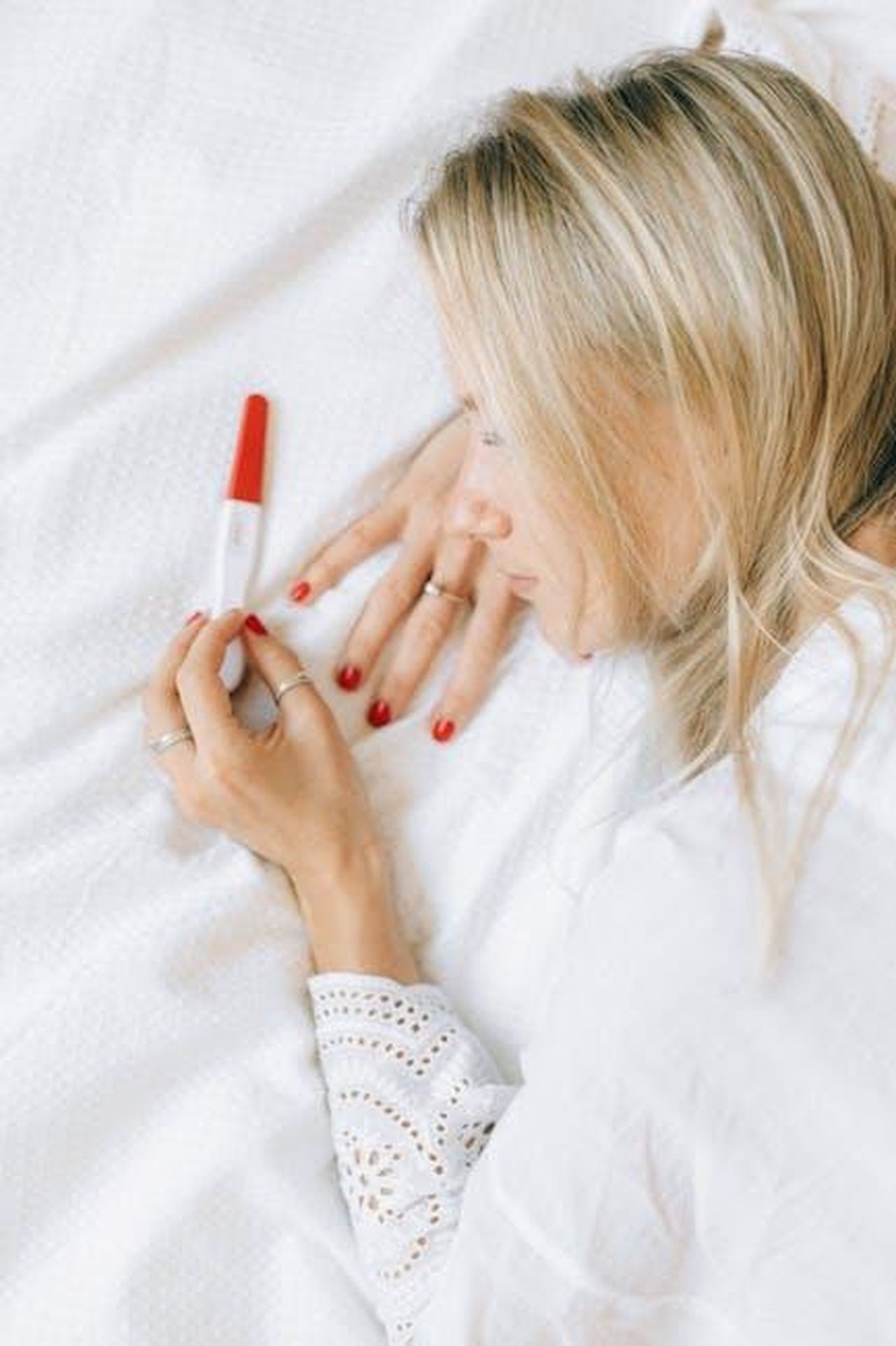 Annuncio_della_gravidanza_di_Michelle_Keegan_NKKugUppXp - Confidenze24 Source: Nataliya Vaitkevich - pexels - A woman lying on a bed looking at a positive pregnancy test with a joyful expression.