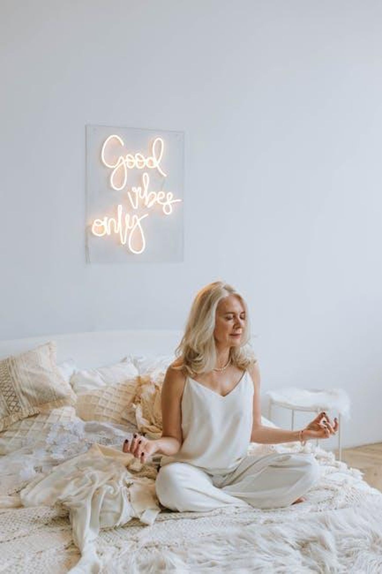 Articoli_per_la_casa_in_saldo_decorazioni_e_accessori_YSIA26Aysa - Confidenze24 Source: Anastasia Shuraeva - pexels - Serene woman meditating on a cozy bed under 'Good Vibes Only' neon sign.
