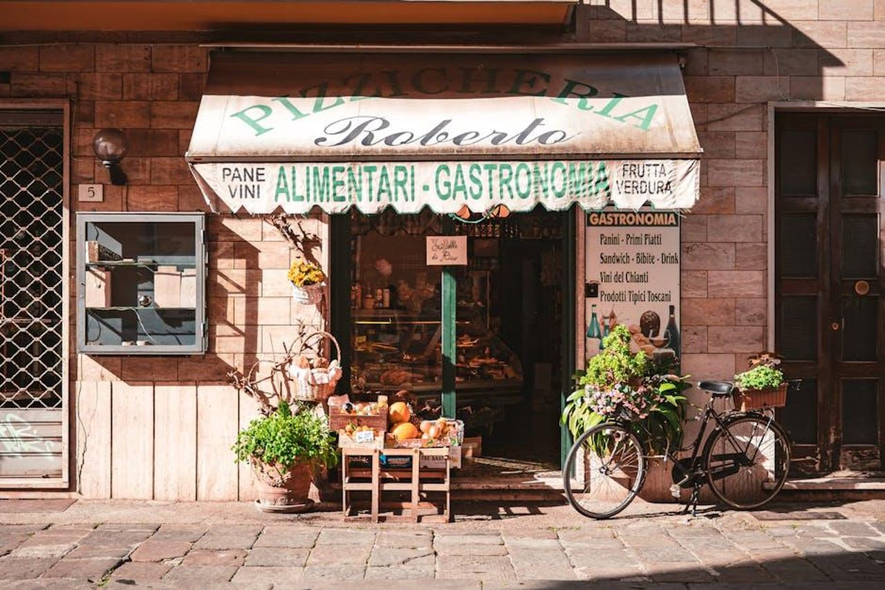Aumenti_percentuali_nelle_ricerche_di_ingredienti_specifici_bQWiUQokXz - Confidenze24 Source: Gonzalo Facello - pexels - A quaint Italian grocery store with fresh produce and a vintage bicycle outside, offering local delicacies.