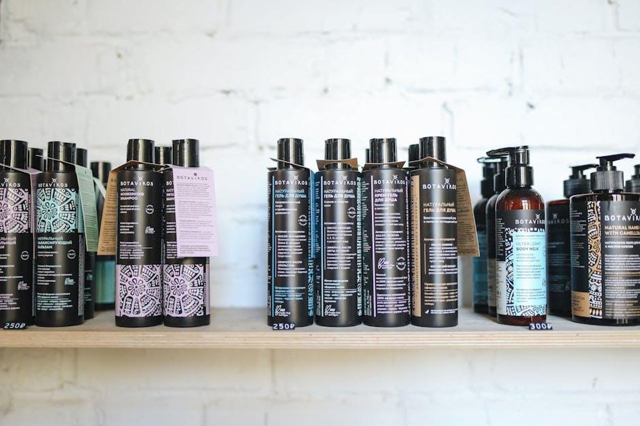 Balsamo_Densifying_di_Oribe_un_musthave_per_capelli_diradati_1vl7jOEdKy - Confidenze24 Source: Polina Tankilevitch - pexels - A variety of natural cosmetic bottles lined up on a wooden shelf against a white brick wall, suggesting eco-friendly beauty.