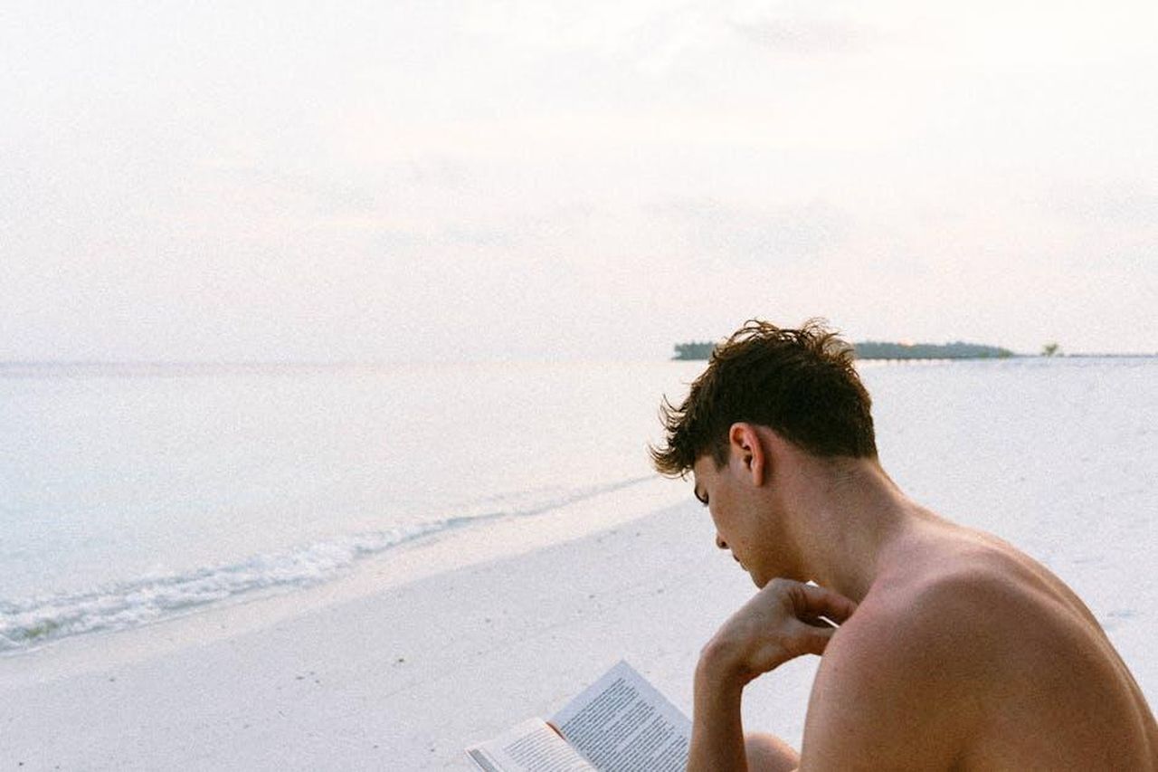 Bill_Rancic_Autore_di_successo_9H0LmrkMj9 - Confidenze24 Source: Martin Péchy - pexels - A man enjoys reading a book on a serene Maldives beach, capturing the essence of relaxation.