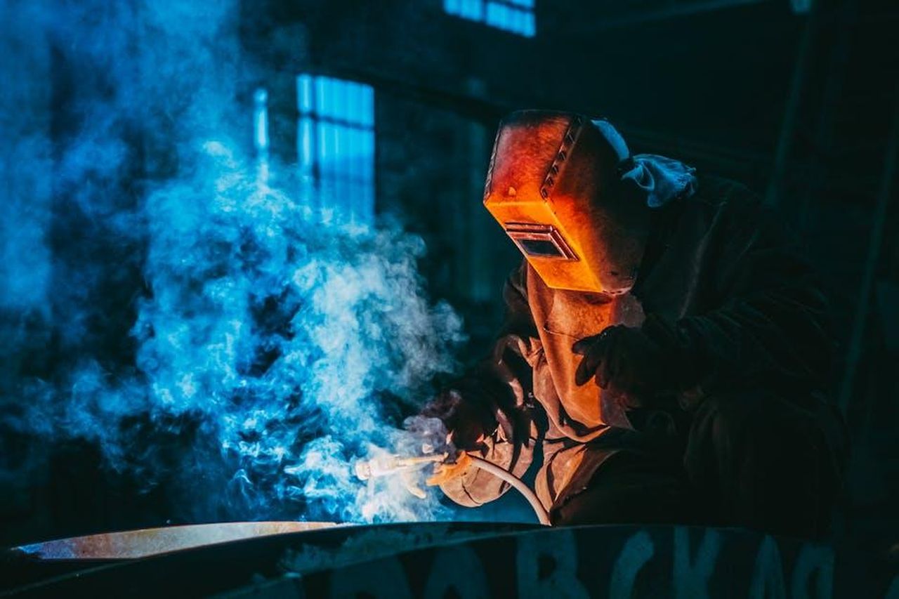 Bill_Rancic_Il_vincitore_della_prima_stagione_di_The_Apprentice_zqhsEMojib - Confidenze24 Source: Kateryna Babaieva - pexels - A welder in a workshop using safety gear to weld metal, surrounded by blue smoke and atmospheric lighting.