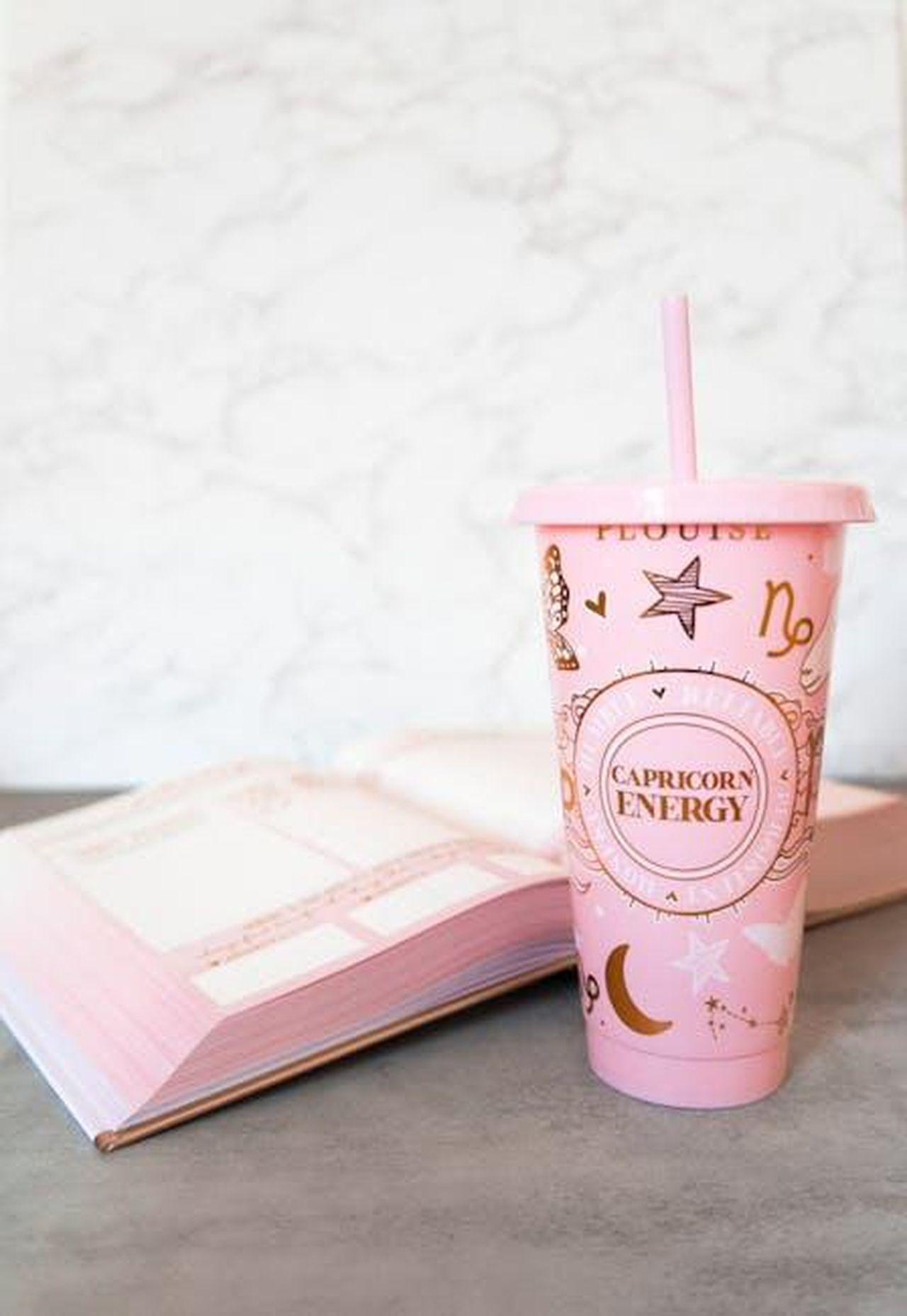 Capricorno_22_dicembre__19_gennaio_AMyS0FPtKe - Confidenze24 Source: Alena Chuyankova - pexels - A pink cup with a straw and astrology design next to an open book on a white background.