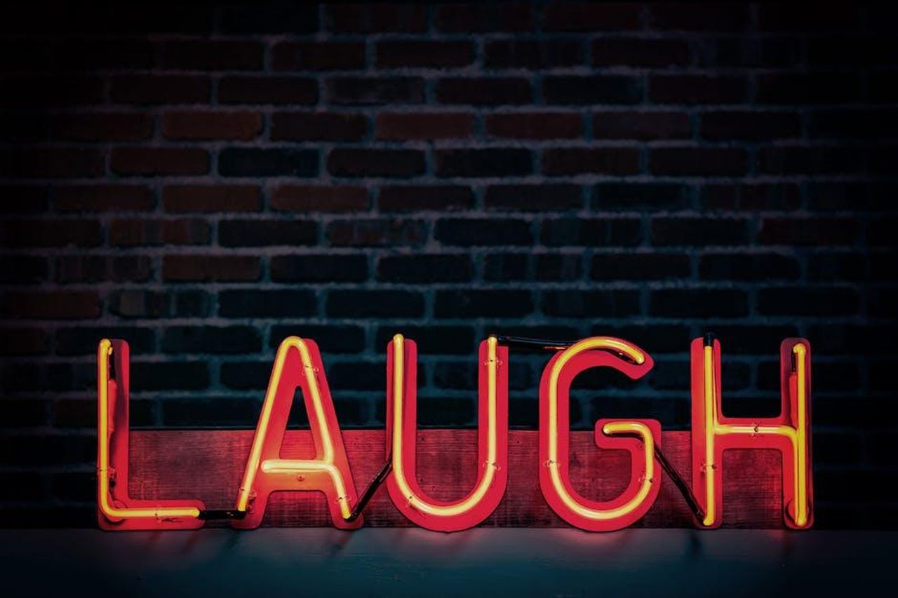 Carl_aveva_un_grande_senso_dellumorismo_2Xpt2QGPpm - Confidenze24 Source: Tim Mossholder - pexels - Bright neon sign displaying 'LAUGH' against a dark brick wall, creating a vibrant mood.