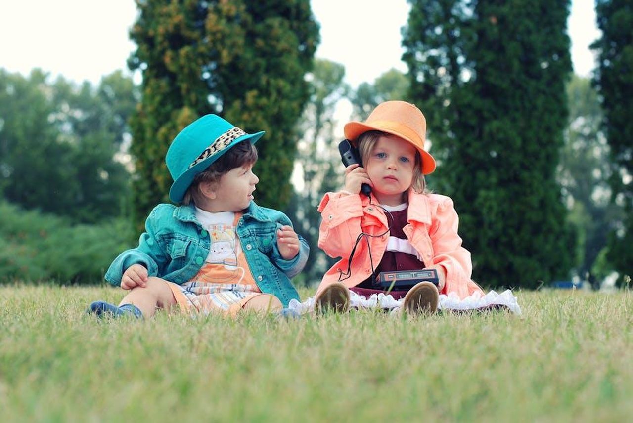 Carl_sapeva_che_Dolly_era_quella_giusta_T3swfFW9MI - Confidenze24 Source: Pixabay - pexels - Two toddlers in colorful outfits enjoying playtime with walkie talkies in a sunny park setting.
