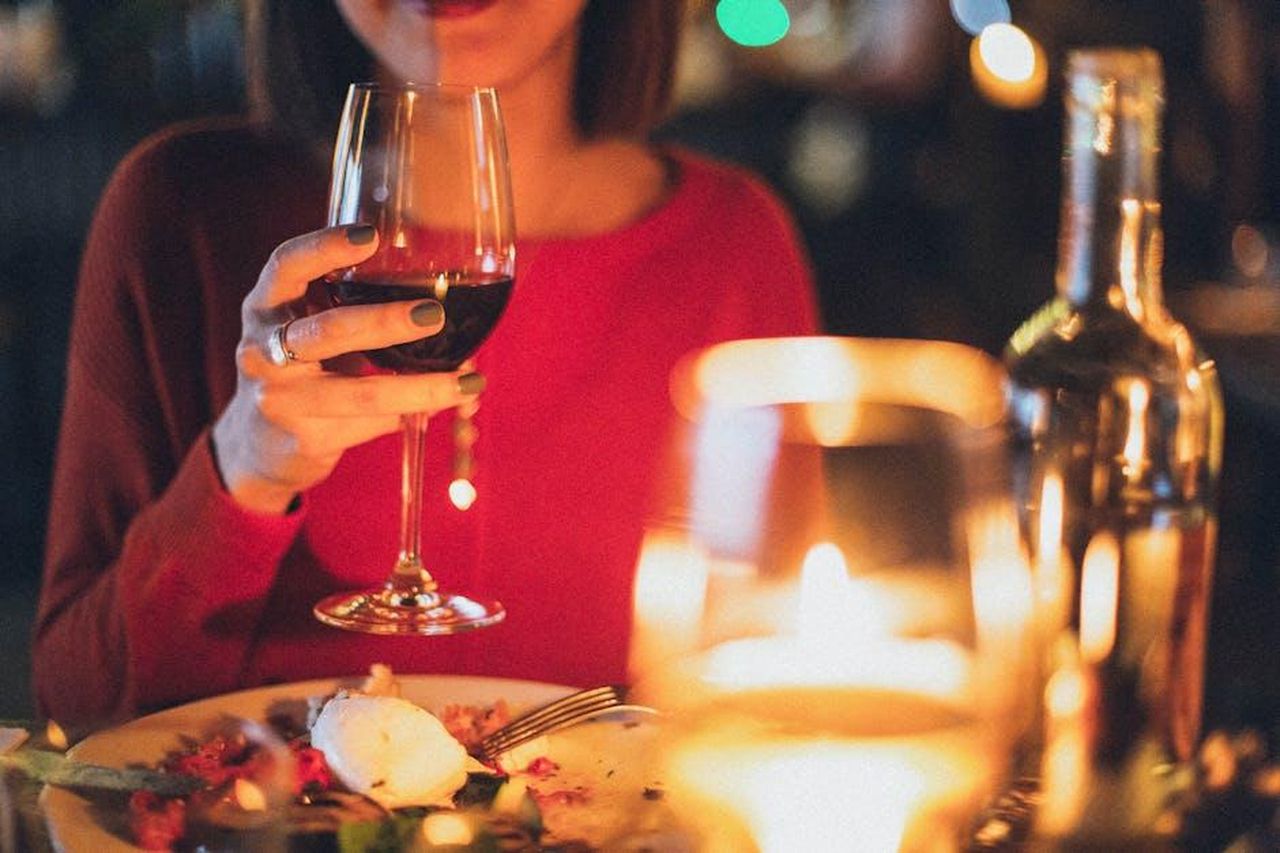 Cene_romantiche_con_Harry_NsVNIyqoQt - Confidenze24 Source: Elina Sazonova - pexels - A woman enjoying red wine at a romantic candlelit dinner, perfect for celebrations.