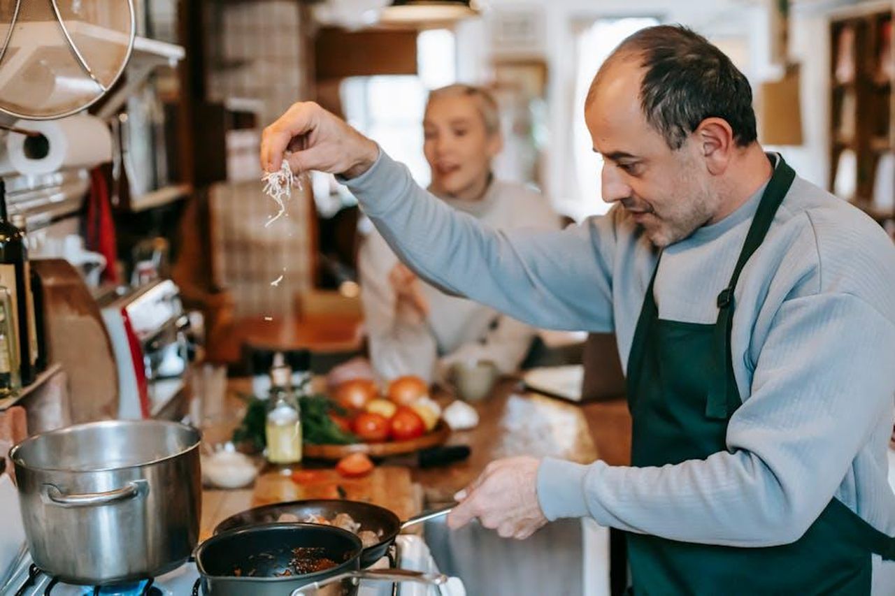 Chris_ottiene_Amanda_dopo_lorario_ma_questo_sta_diventando_raro_snNXch8ubo - Confidenze24 Source: Gary Barnes - pexels - Focused male in apron adding ingredient into frying pan heating on gas stove while cooking meal for woman