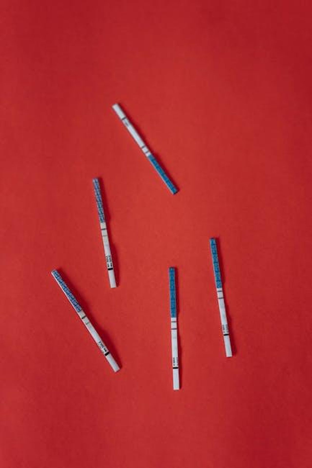 Ci_sono_sintomi_n8PRoLl3ZL - Confidenze24 Source: olia danilevich - pexels - Multiple pregnancy test strips scattered on a vibrant red backdrop, symbolizing fertility and anticipation.