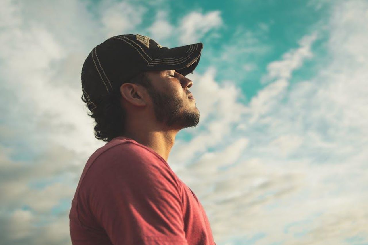 Coinvolgi_i_Tuoi_Sensi_per_Minimizzare_lo_Stress_Uq39UmY9rc - Confidenze24 Source: Kelvin Valerio - pexels - A man enjoys outdoor relaxation and mindfulness beneath a bright, cloudy sky, exuding calm and peace.