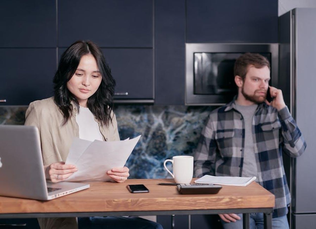 Coinvolgimento_di_Iain_Rawlinson_ZloOfjGcKL - Confidenze24 Source: Mikhail Nilov - pexels - Asian woman and Caucasian man reviewing bills and discussing finances in a modern kitchen setting.