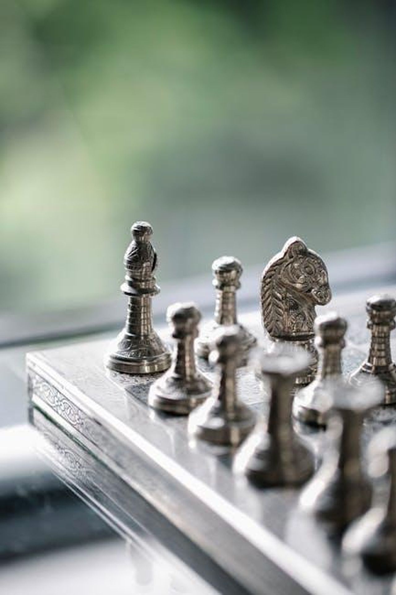 Collezione_Completa_di_Hunger_Games_xs2O5oXDfz - Confidenze24 Source: Alex Green - pexels - A detailed close-up of a metal chess set on a reflective surface with a blurred green background.