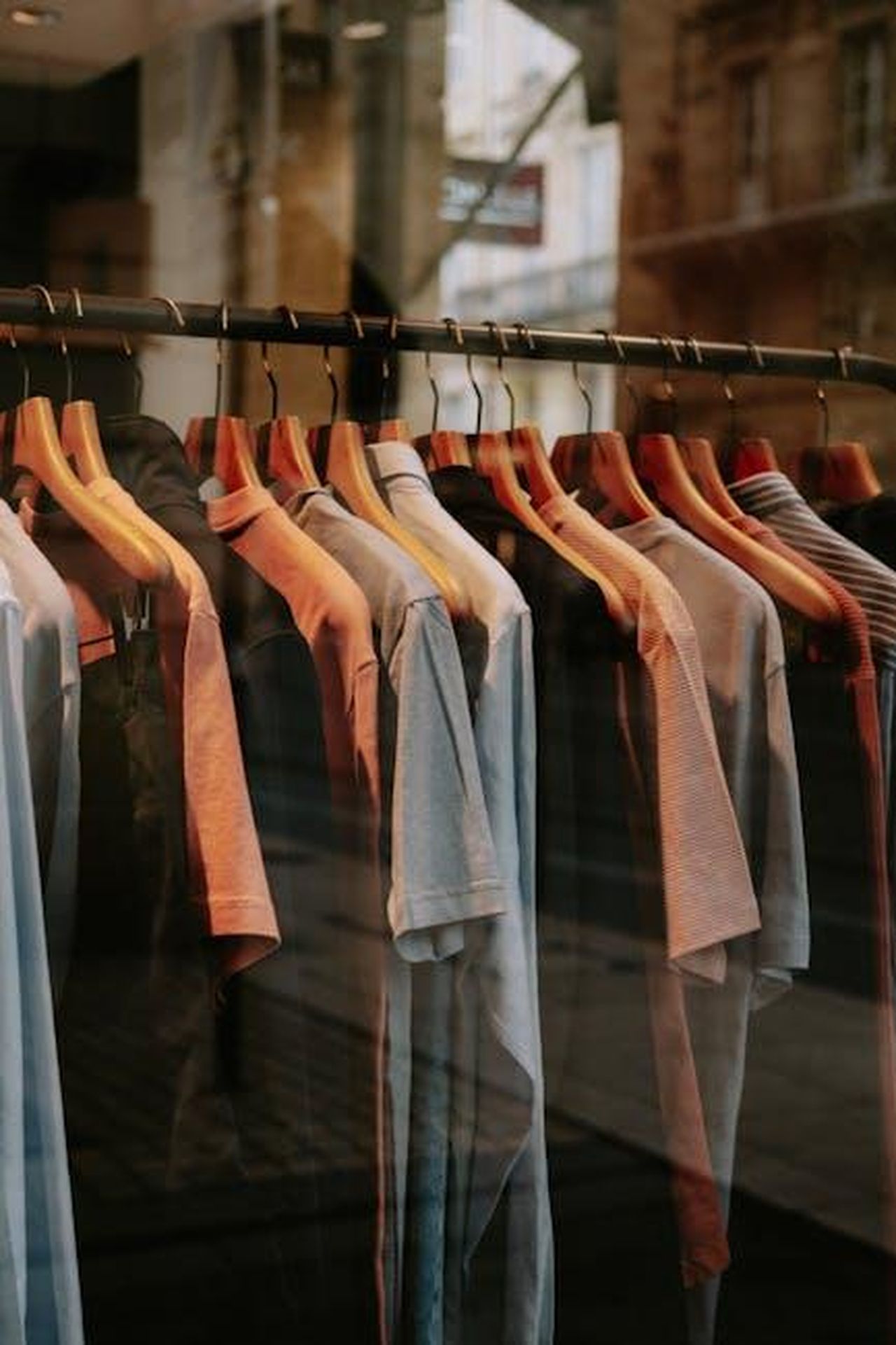 Collezione_primaverile_di_Little_Sleepies_0FoVnDu3Qh - Confidenze24 Source: Mathias Reding - pexels - A collection of shirts on wooden hangers displayed in a storefront window, showcasing fashion style.