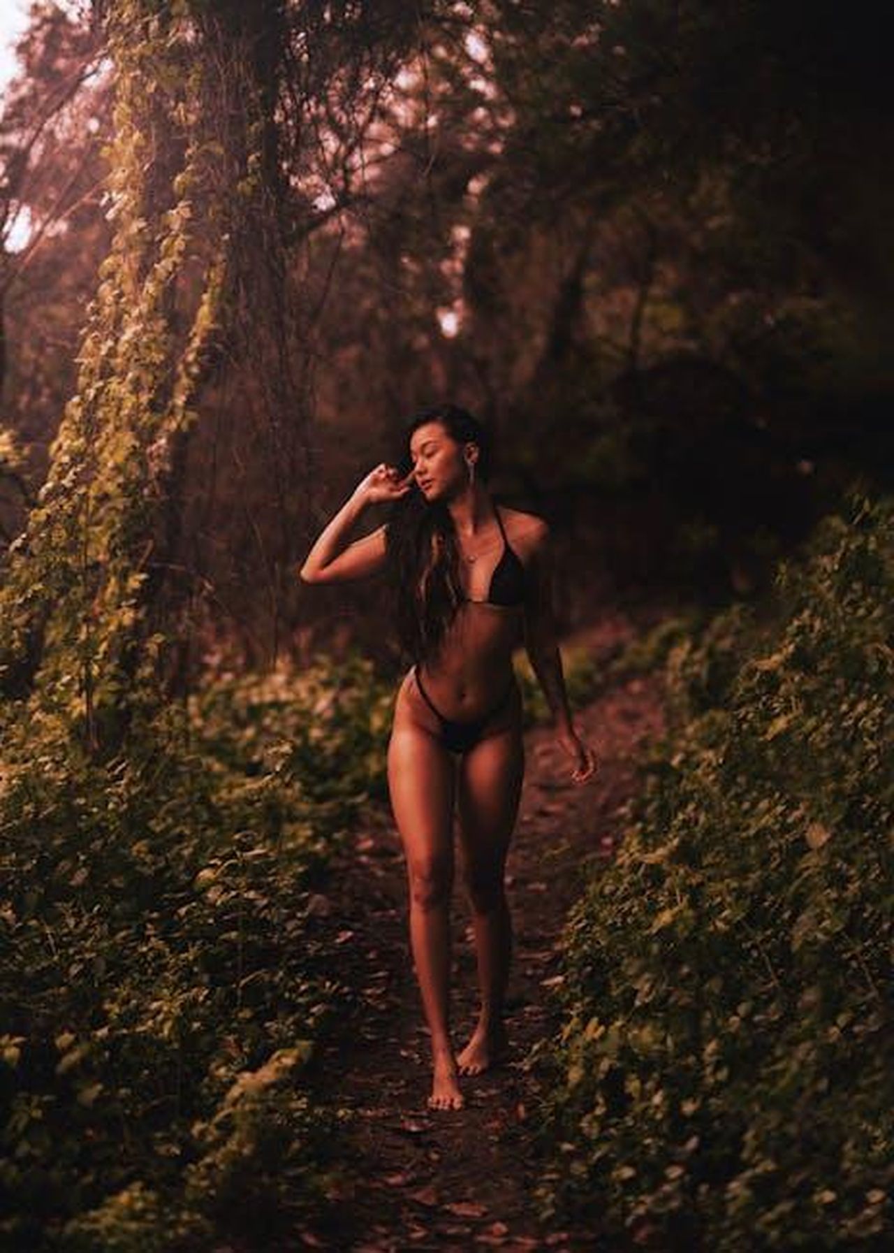 Come__stato_scoperto_il_corpo_di_Pamela_Wi39c1HytN - Confidenze24 Source: pedro furtado - pexels - A woman in a bikini walking barefoot through a verdant forest path, surrounded by greenery.
