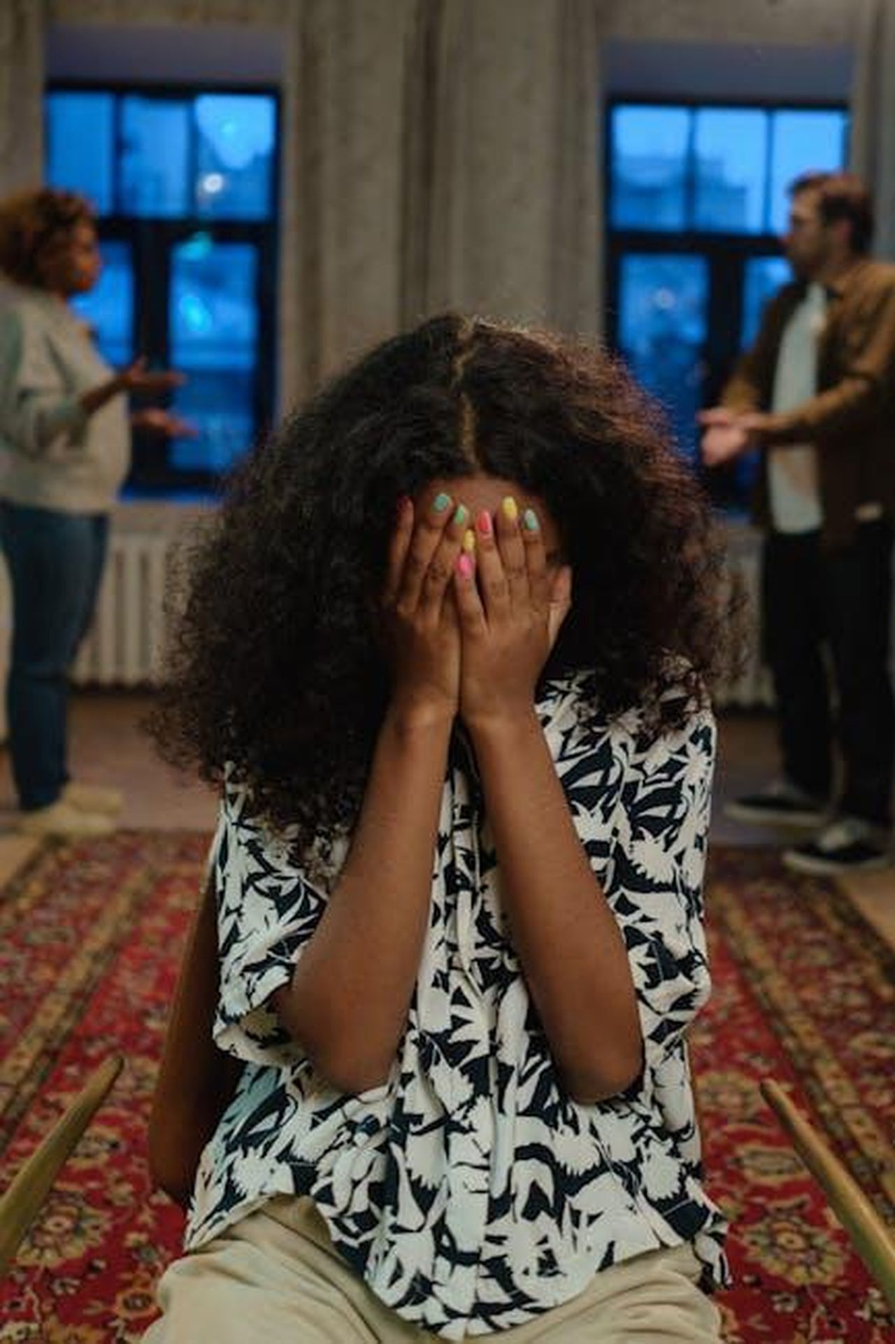 Commenti_di_esperti_sulla_privacy_della_famiglia_reale_0snG1CM9hp - Confidenze24 Source: cottonbro studio - pexels - A young woman sits indoors with her face covered amidst a family argument, conveying distress and conflict.