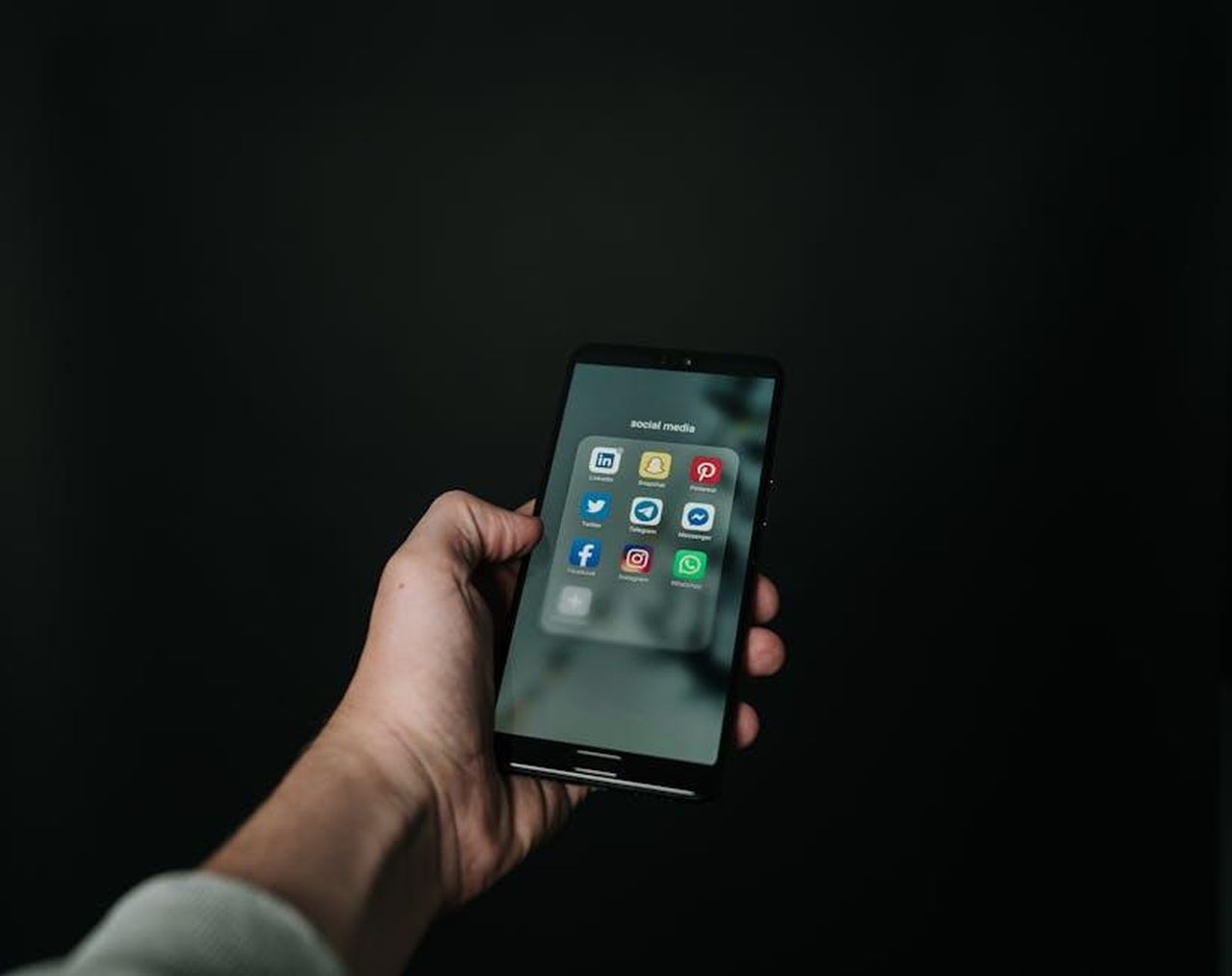 Commenti_entusiasti_sui_social_RGbUFsuN8v - Confidenze24 Source: Magnus Mueller - pexels - Close-up of a hand holding a smartphone displaying various social media app icons on a dark background.