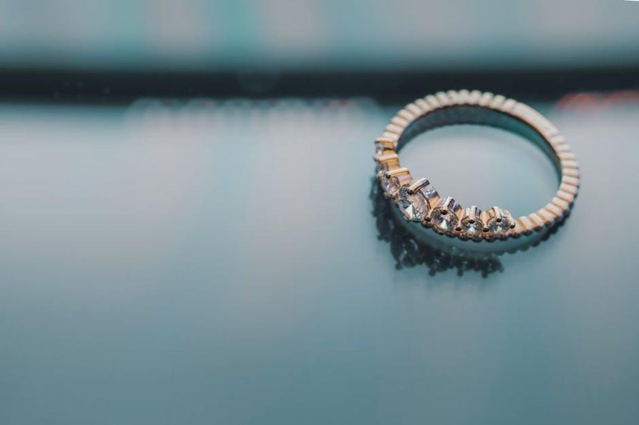 Confronto_tra_lanello_di_fidanzamento_e_quello_nuziale_U3c1GJNlT2 - Confidenze24 Source: FOX ^.ᆽ.^= ∫ - pexels - Close-up of a gold ring with diamonds on a reflective surface, showcasing elegance and luxury.