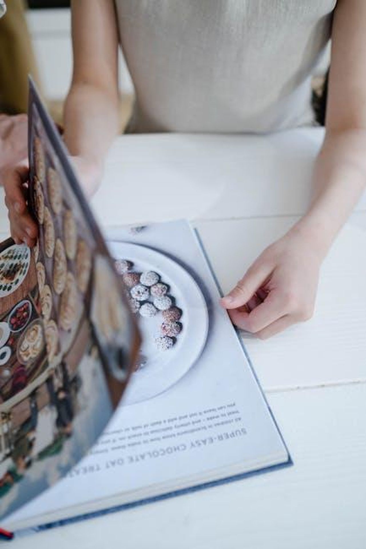 Consigli_di_Martha_per_una_torta_perfetta_EvTRALebac - Confidenze24 Source: Ron Lach - pexels - A person flips through a pastry cookbook showcasing delectable dessert images.