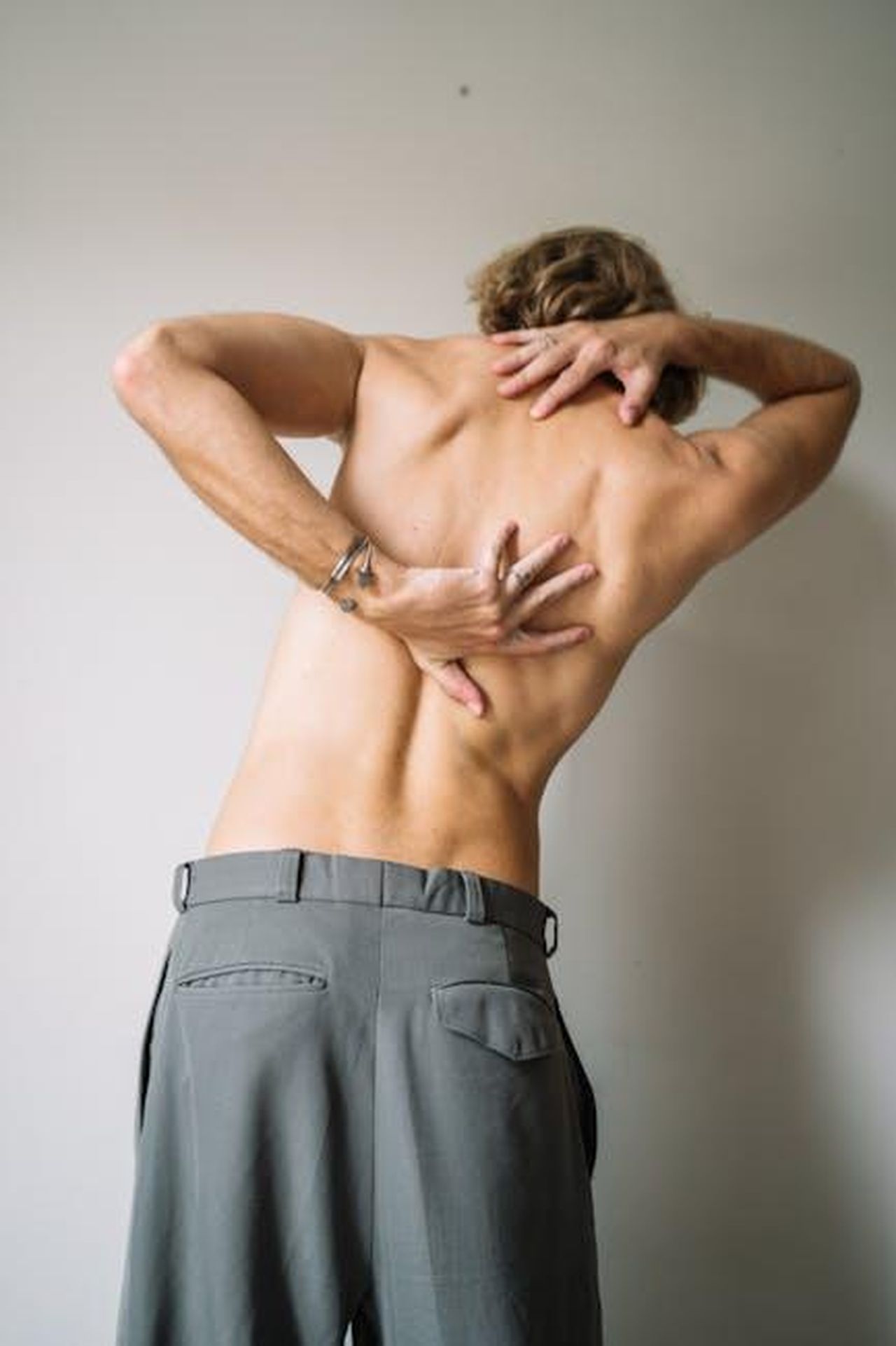 Contesto_della_situazione_di_Wendy_Williams_MV0HgepZUj - Confidenze24 Source: Anna Tarazevich - pexels - A shirtless man stretching his back indoors, showcasing muscular anatomy.