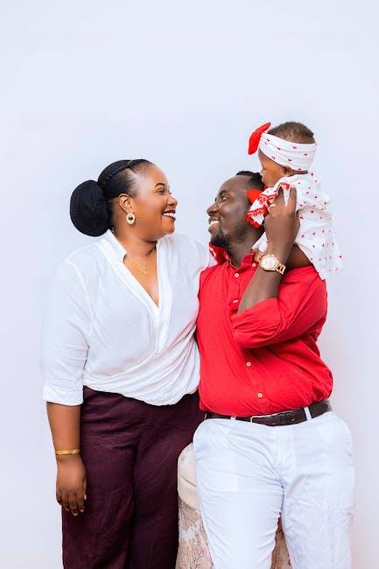 Cos_emozionato_di_vedere_il_suo_viso_JAgUhDX9ib - Confidenze24 Source: Safari Consoler - pexels - Joyful family portrait featuring parents and baby dressed in white and red attire against a light background.