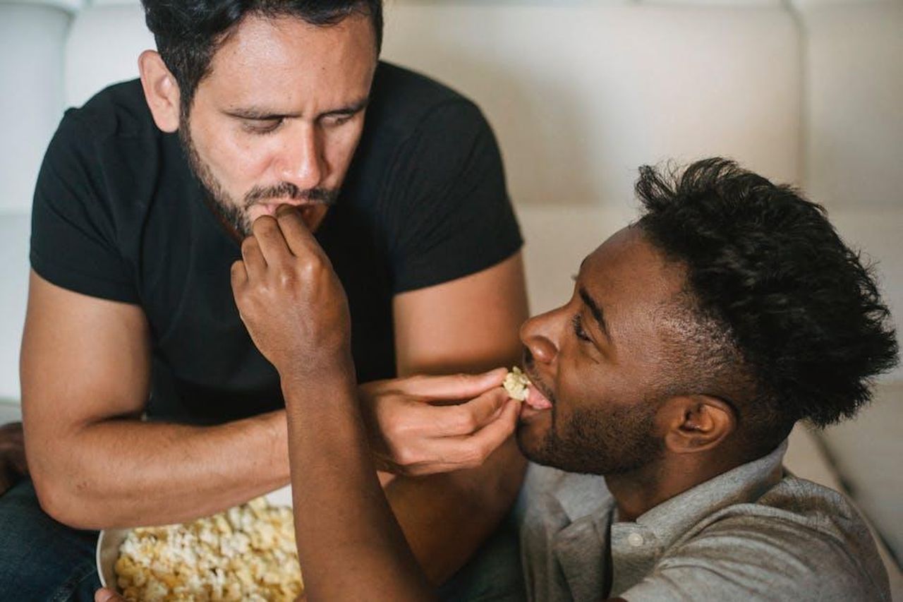 Cosa_ha_mostrato_il_teaser_del_finale_9fJ9GI2sqm - Confidenze24 Source: Ketut Subiyanto - pexels - Two men sharing popcorn in a cozy indoor setting, showcasing love and affection.