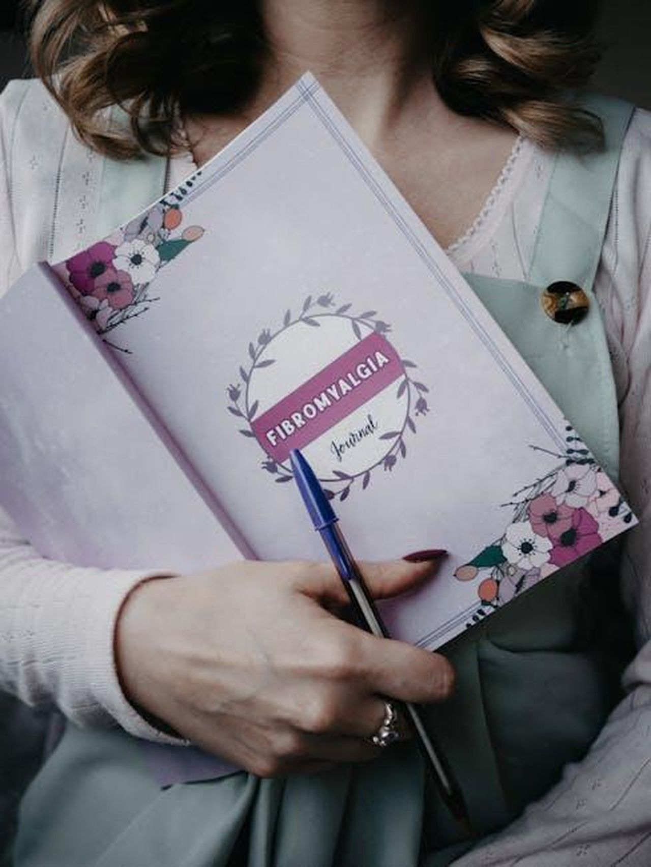 Crescita_personale_e_relazioni_LVH0HQGmrh - Confidenze24 Source: Lisa from Pexels - pexels - A woman holding a fibromyalgia journal with floral design, emphasizing health and awareness.