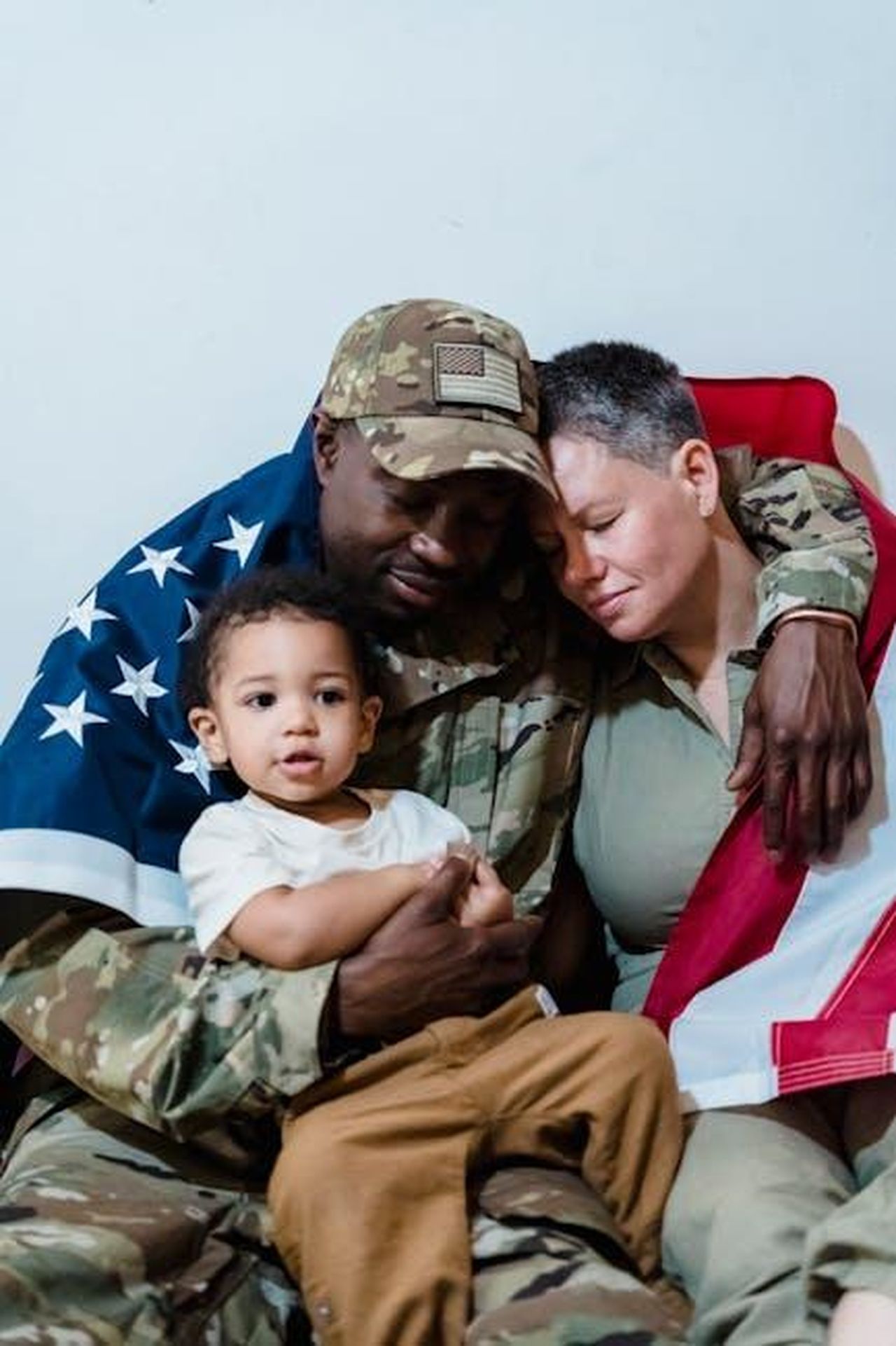 Critiche_alla_presenza_della_moglie_JEX1TmNXTu - Confidenze24 Source: George Pak - pexels - Emotional family reunion with a soldier wrapped in an American flag, embracing loved ones.