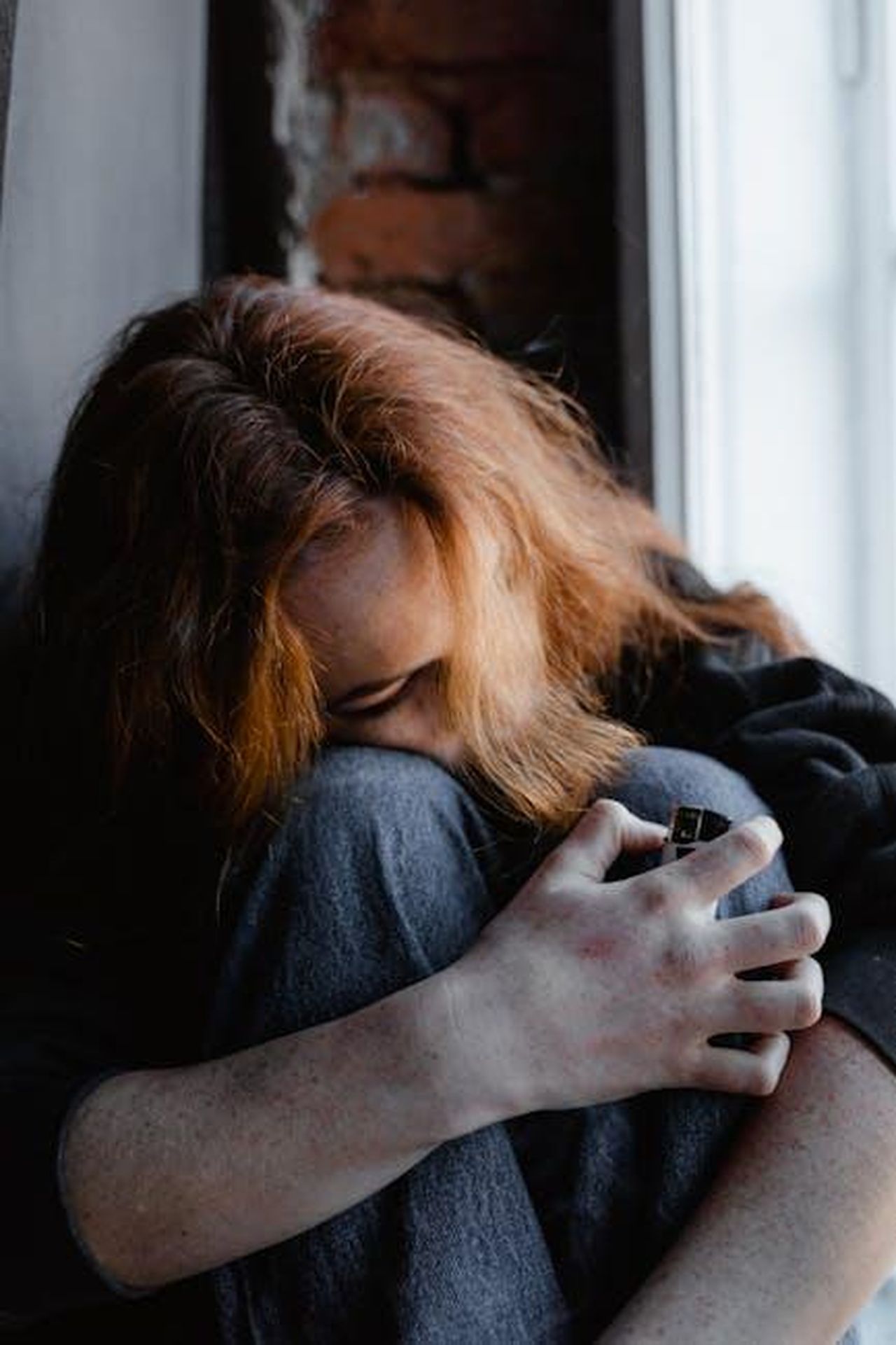 Critiche_alla_serie_e_alla_gestione_del_dolore_Dld2HKdkgz - Confidenze24 Source: MART PRODUCTION - pexels - A woman showing signs of distress while seated indoors against a brick wall, holding her knees.