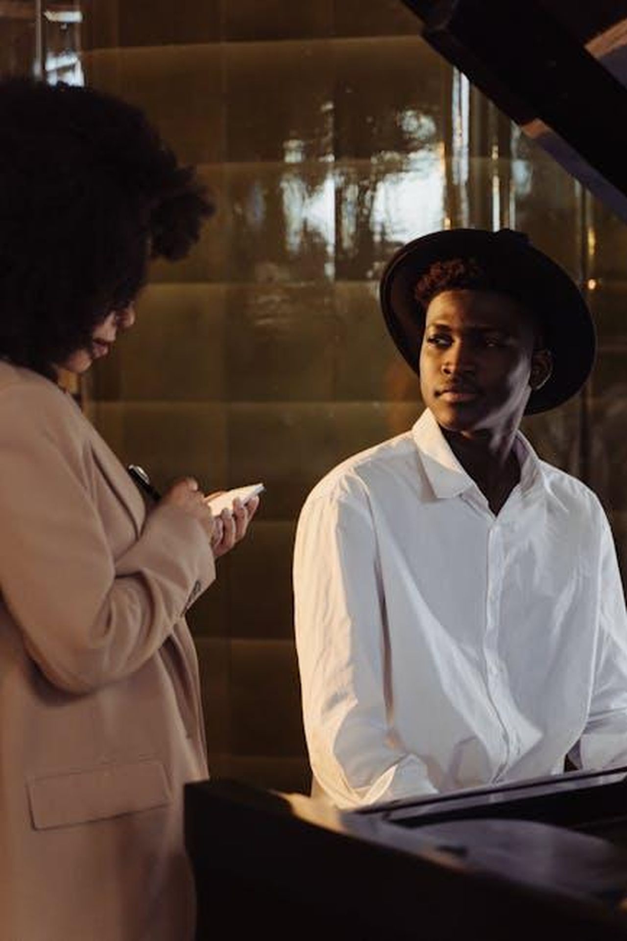 Critiche_alle_domande_sulla_musica_Ok9RWrlITQ - Confidenze24 Source: cottonbro studio - pexels - A musician in a hat sits at a piano while a woman takes notes during an interview indoors.