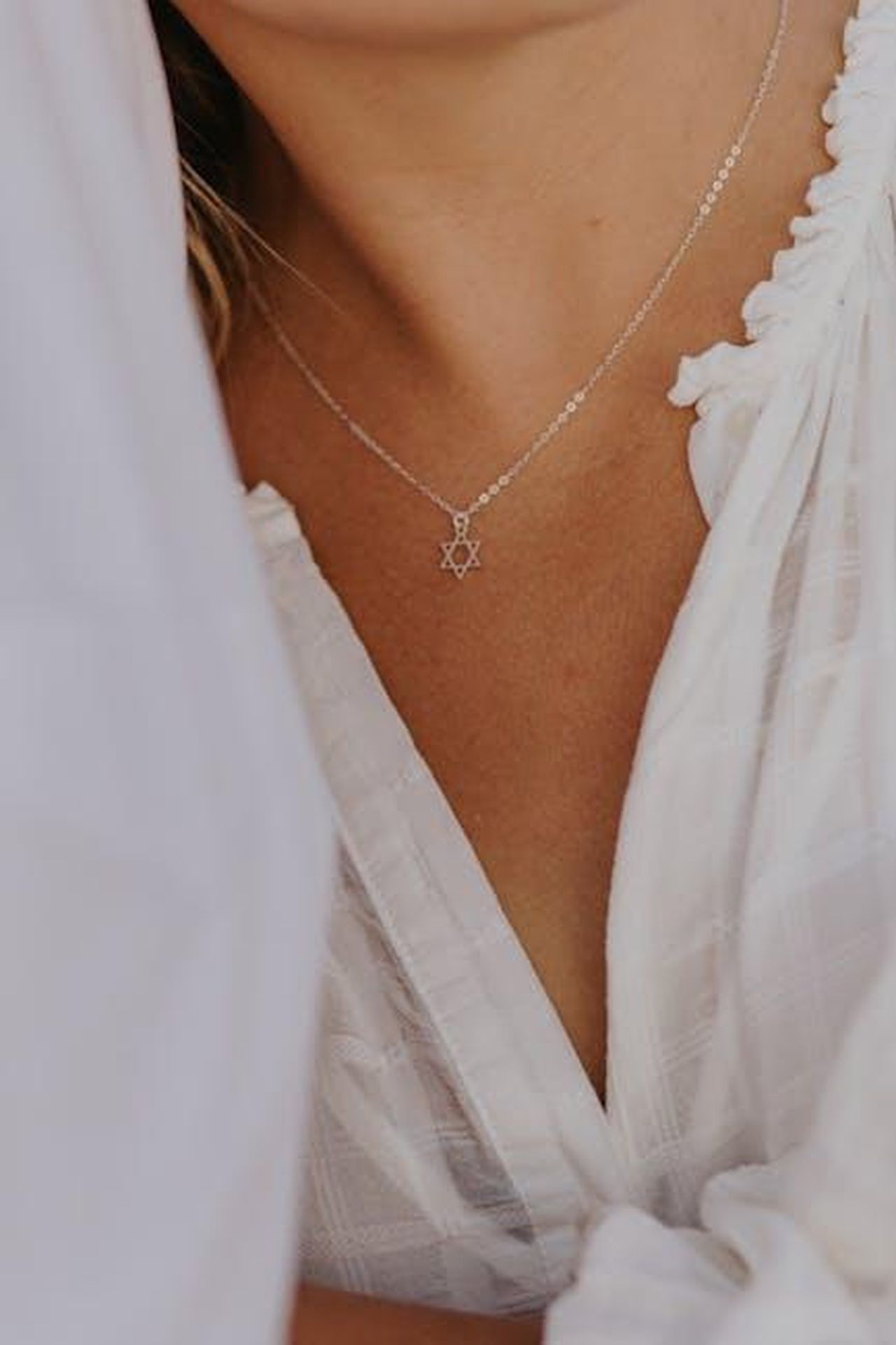 Critiche_per_loutfit_di_David_Potts_Rt2B9U0CFC - Confidenze24 Source: RDNE Stock project - pexels - Close-up of a woman wearing a silver Star of David necklace and a white blouse.