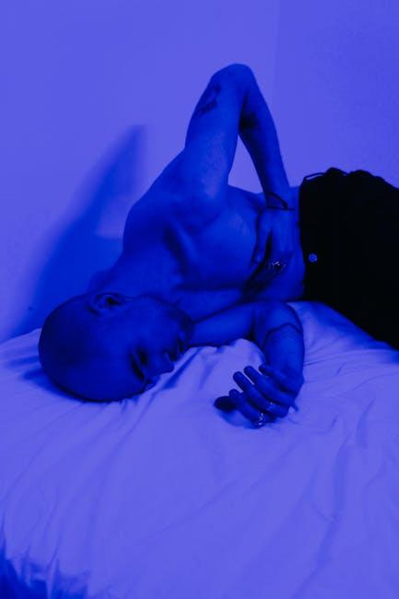 Cuore_spezzato_per_Georgia_7HopY6jkQs - Confidenze24 Source: cottonbro studio - pexels - A shirtless man lies on a bed in blue light, expressing deep emotion and contemplation.