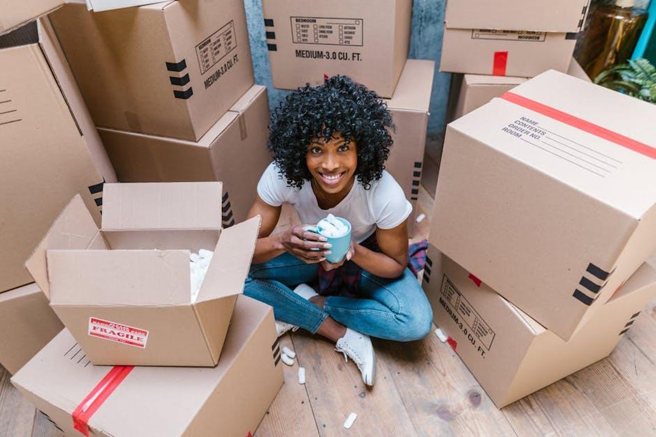 Danny_e_Georgia_vogliono_andare_avanti_LuPrJXtmEl - Confidenze24 Source: RDNE Stock project - pexels - A woman sitting among moving boxes with a mug, surrounded by packing materials.
