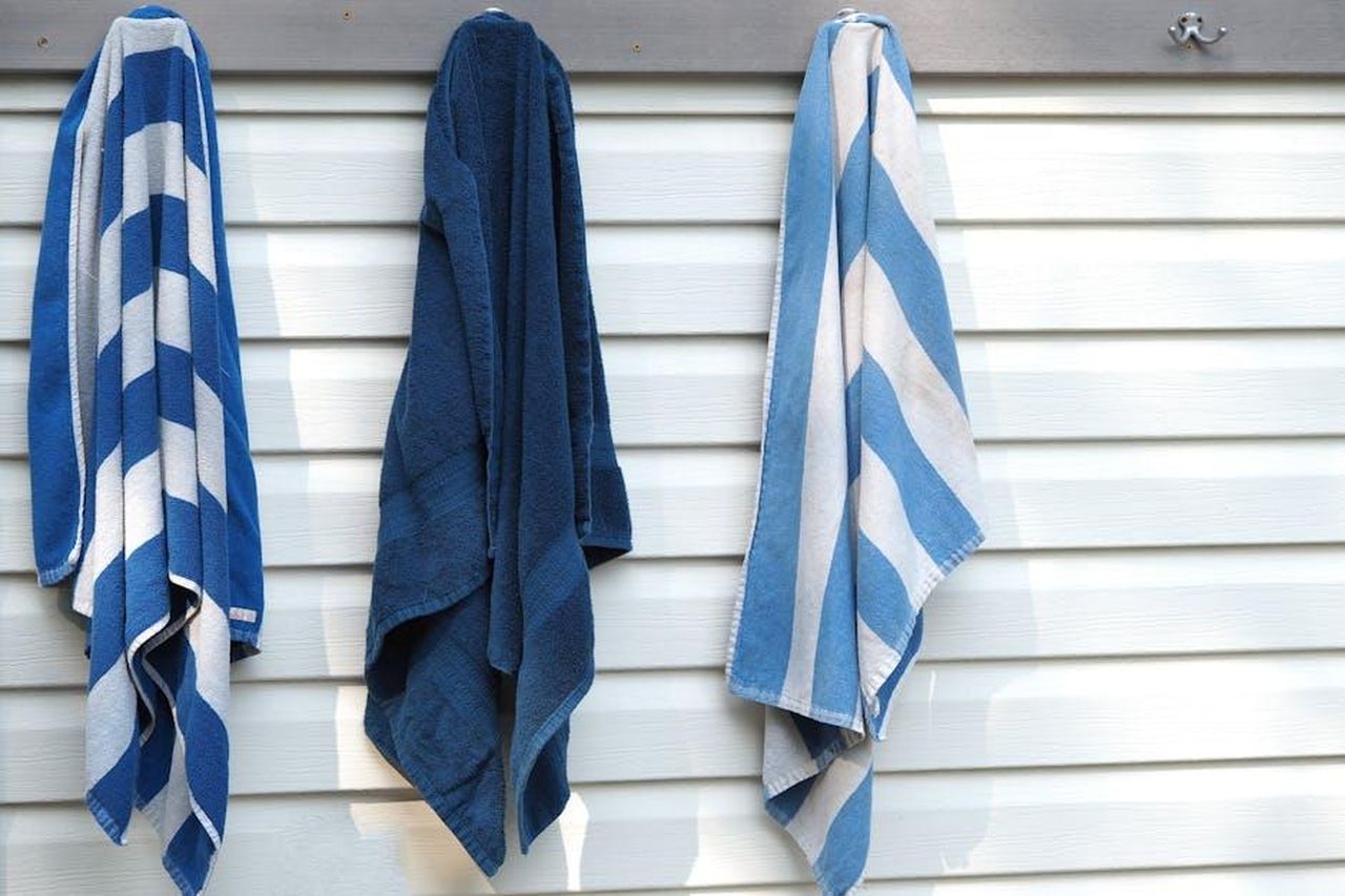 Design_e_praticit_dei_teli_Sun_Squad_QSvfddLhJ3 - Confidenze24 Source: Gene Samit - pexels - Three blue and white striped towels hanging on an exterior wall in sunlight.