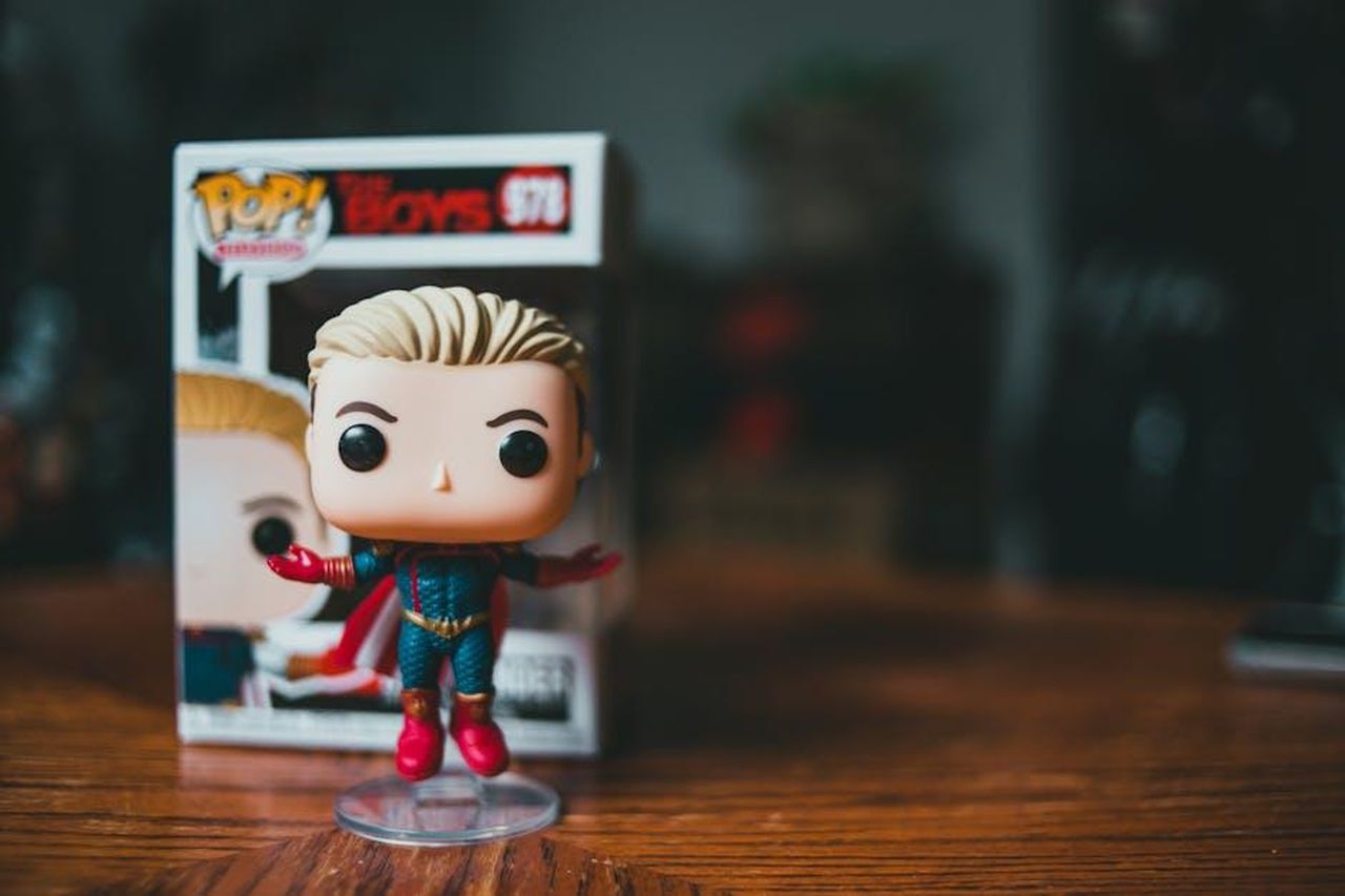 Dettagli_su_Vought_Rising_e_il_cast_mlYJFWcVna - Confidenze24 Source: Erik Mclean - pexels - A vibrant collectible character toy figurine standing in front of its packaging on a wooden table.