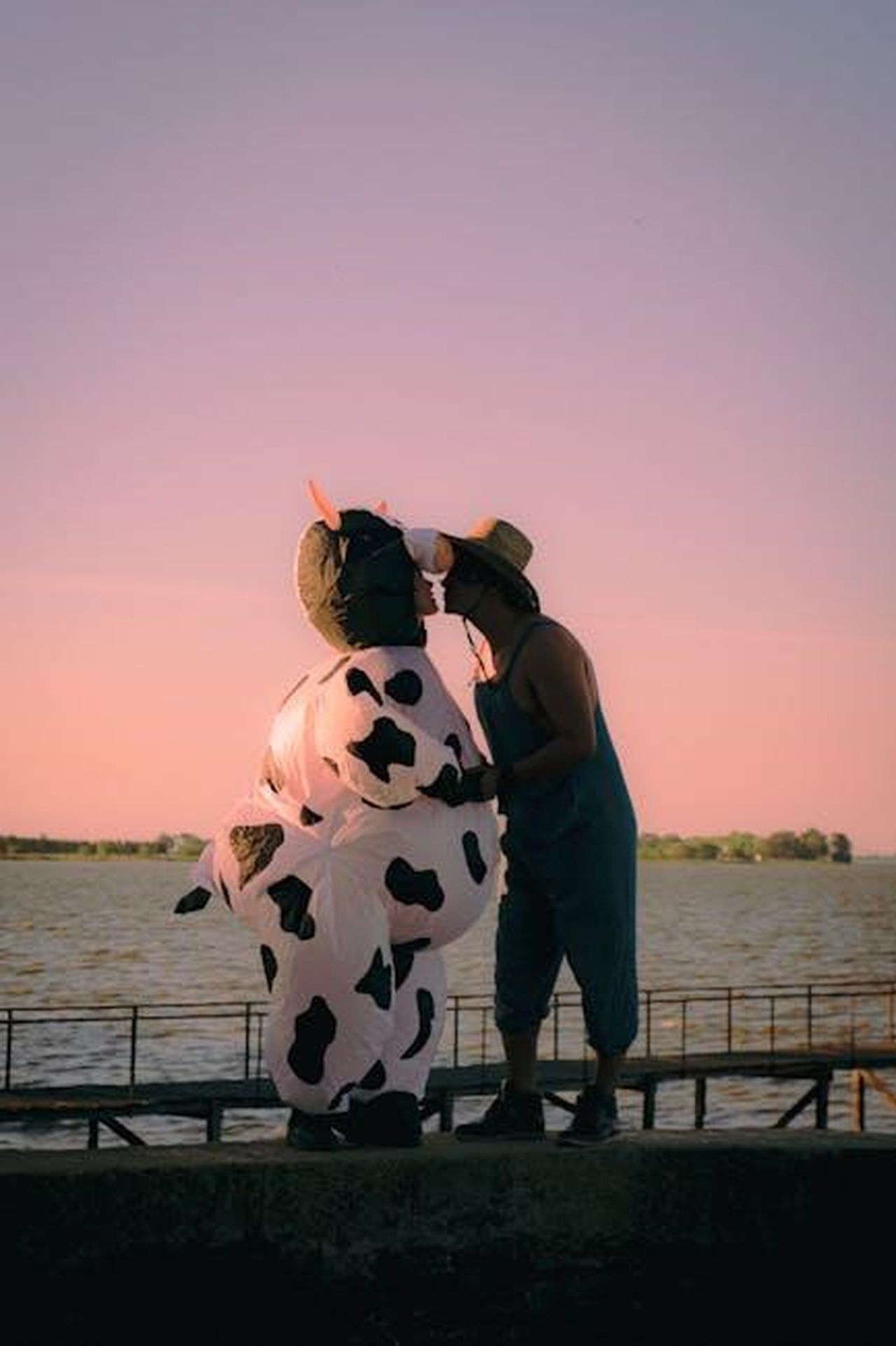Dettagli_sul_film_Office_Romance_a24r3YWFEh - Confidenze24 Source: Agustina Tolosa - pexels - A playful scene at sunset featuring a person in a cow costume by a lakeside, capturing a moment of joy and fun.