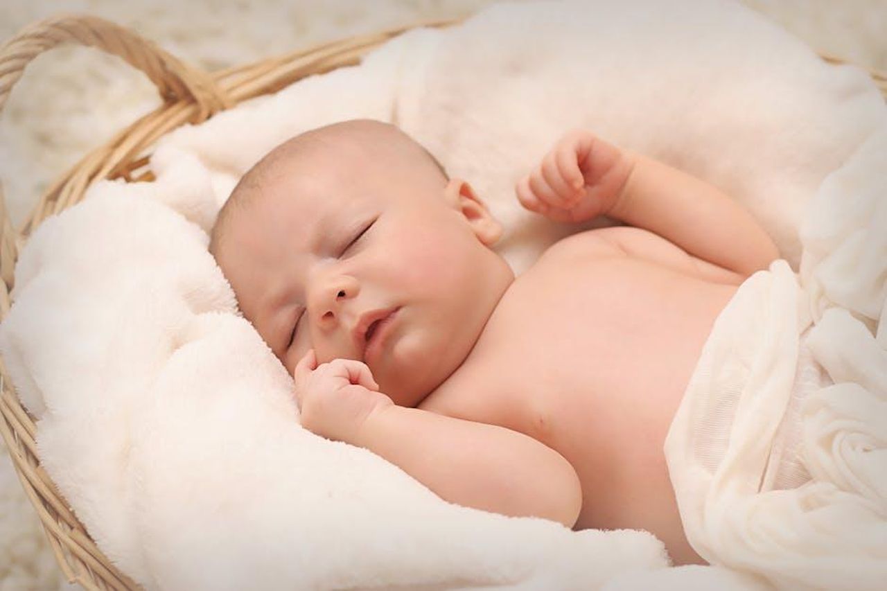 Dettagli_sulla_nascita_del_loro_bambino_07Y8j46sh4 - Confidenze24 Source: Pixabay - pexels - A peaceful sleeping baby nestled in a soft, fluffy blanket inside a wicker basket.