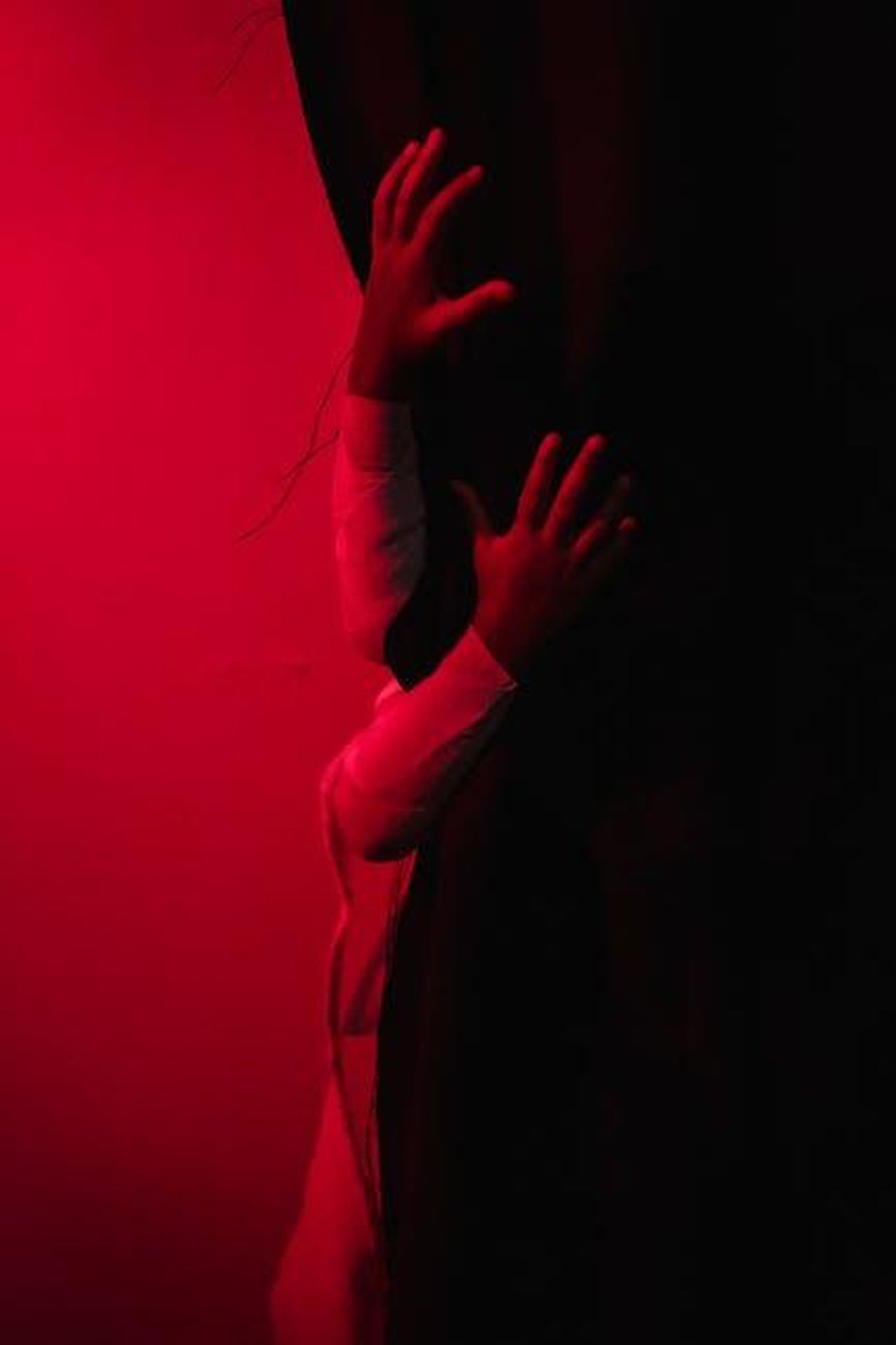 Dettagli_sulla_vita_privata_di_Elisabeth_Moss_TV5TZoYivX - Confidenze24 Source: Mike Jones - pexels - Mysterious image featuring hands gripping a dark curtain under red light, evoking suspense.
