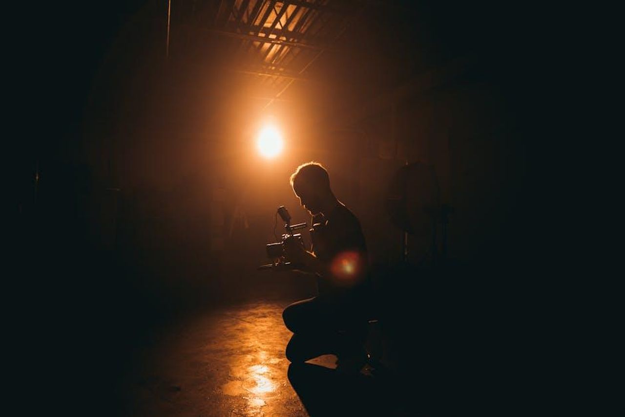 Dettagli_sullincidente_mortale_e_le_conseguenze_legali_ssxrY5qqYw - Confidenze24 Source: Kyle Loftus - pexels - Silhouette of a cinematographer operating a camera in a dimly lit studio with dramatic lighting.