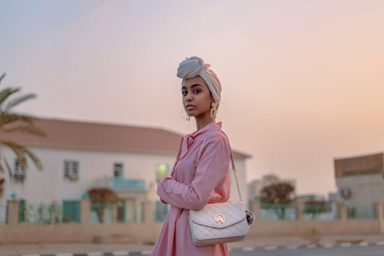 Diagnosi_nel_2005_ZpNKECV1bG - Confidenze24 Source: Ahmed Satti - pexels - Stylish woman in pink dress with turban, posing outdoors at sunset.