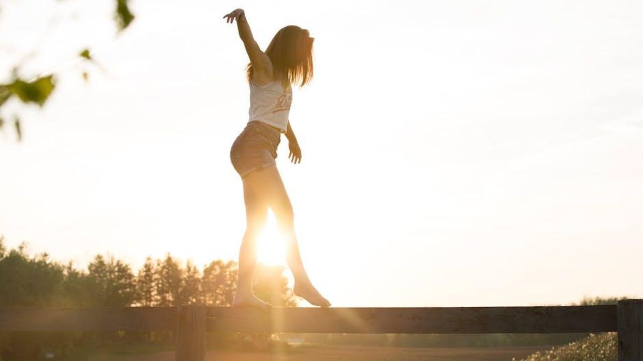 Difficile_bilanciare_tutto_6jWBuZlS4E - Confidenze24 Source: Sebastian V. - pexels - A young woman balancing on a fence during a serene sunrise, exuding freedom and joy.