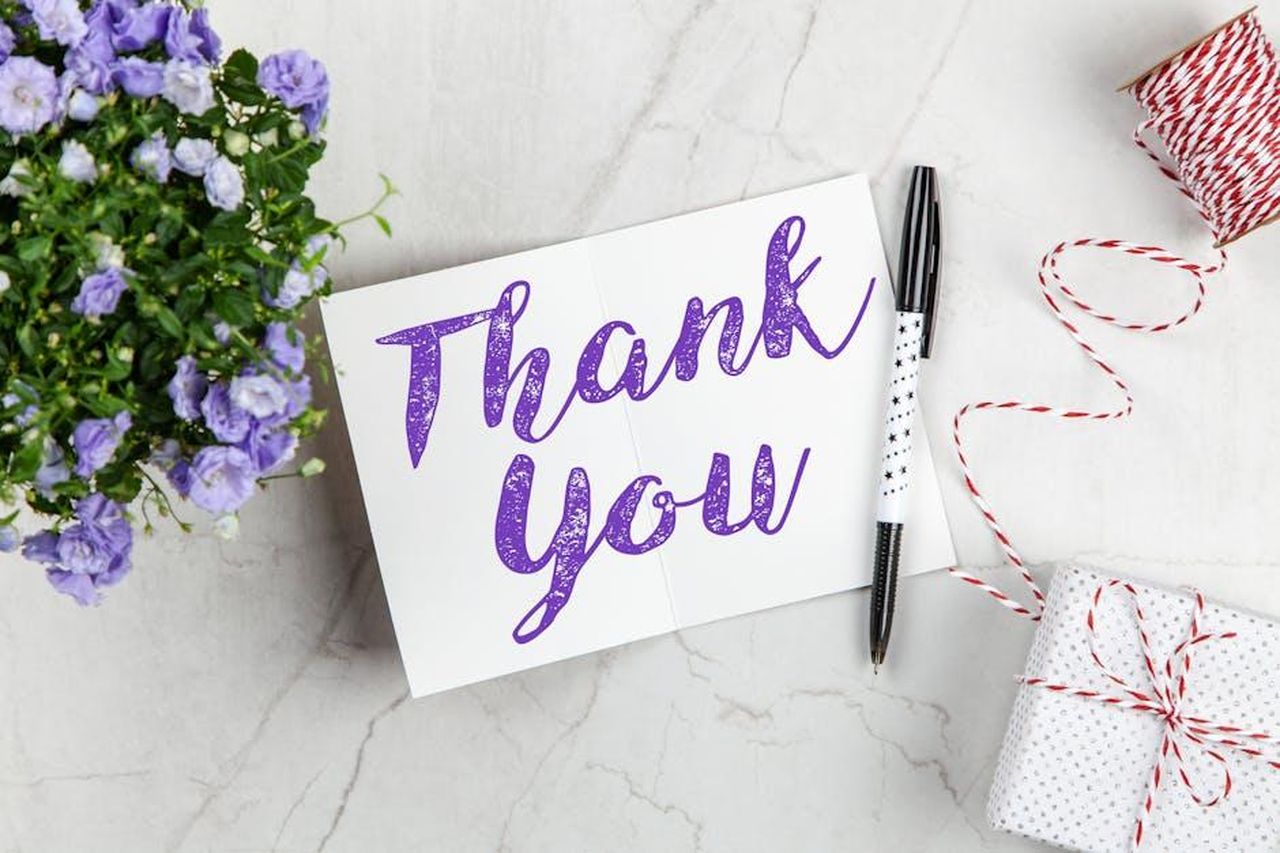 Doechii_esprime_gratitudine_a_Lauryn_Hill_IXw2rTZ5yY - Confidenze24 Source: George Dolgikh - pexels - A stylish thank you card paired with purple flowers, a gift box, and pen on a marble surface.
