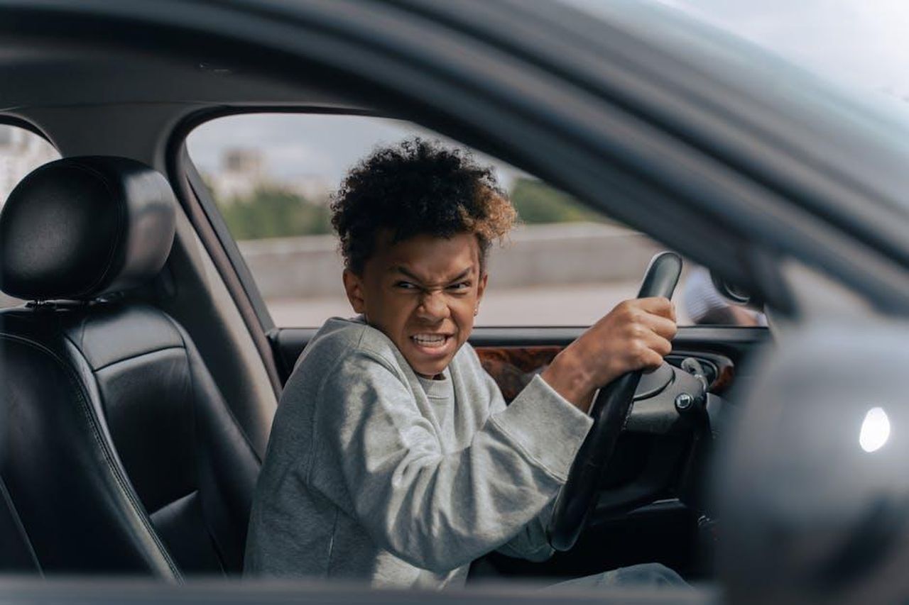 E_quando_finalmente_guidano_Oh_boy_7NoucIFs0f - Confidenze24 Source: Ron Lach - pexels - A teenager in a car momentarily pretending to drive with a determined expression while sitting indoors.