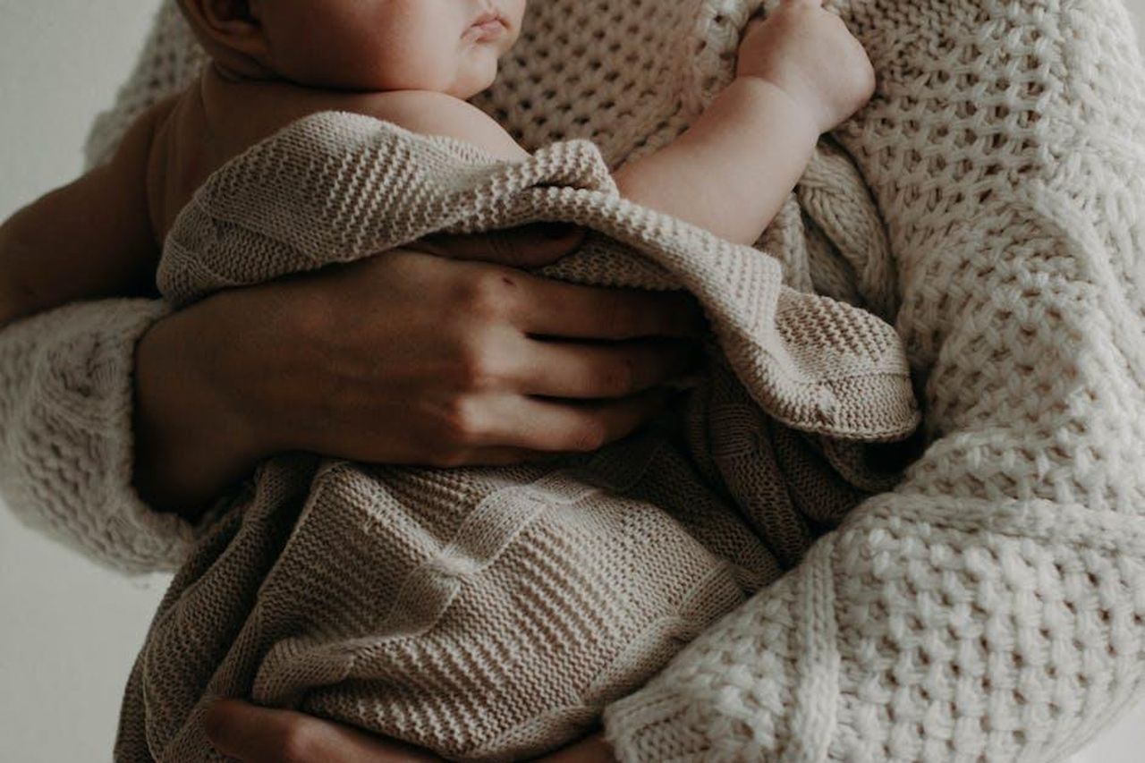 Essere_mamma_e_matrigna_lesperienza_di_Leah_sOMv23WXTC - Confidenze24 Source: Kristina Paukshtite - pexels - A tender moment of a mother holding her baby wrapped in a blanket, exuding warmth and care.