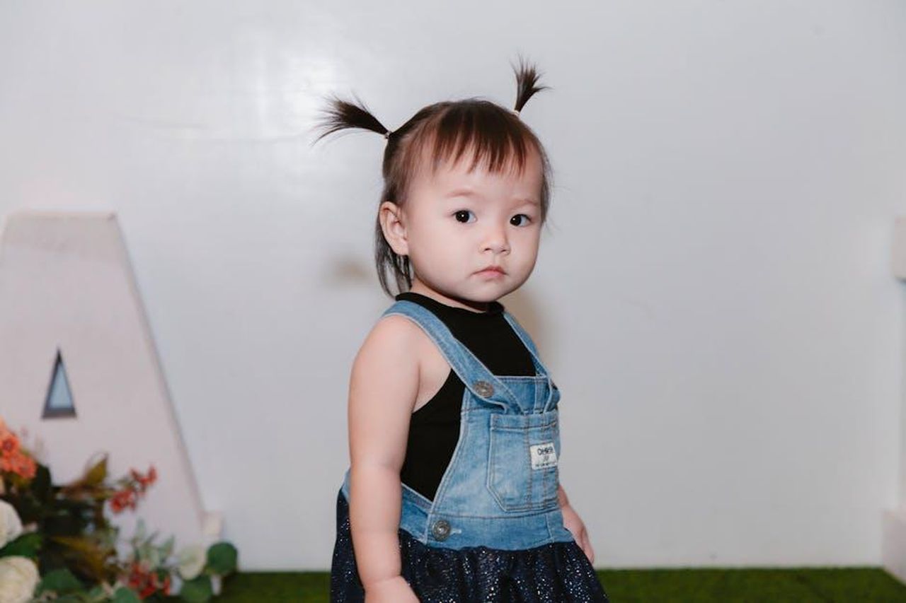 Esti_e_la_moda_la_scelta_delle_scarpe_MxPCVYv8Bf - Confidenze24 Source: Thể Phạm - pexels - Adorable toddler with pigtails wearing a denim dress indoors.