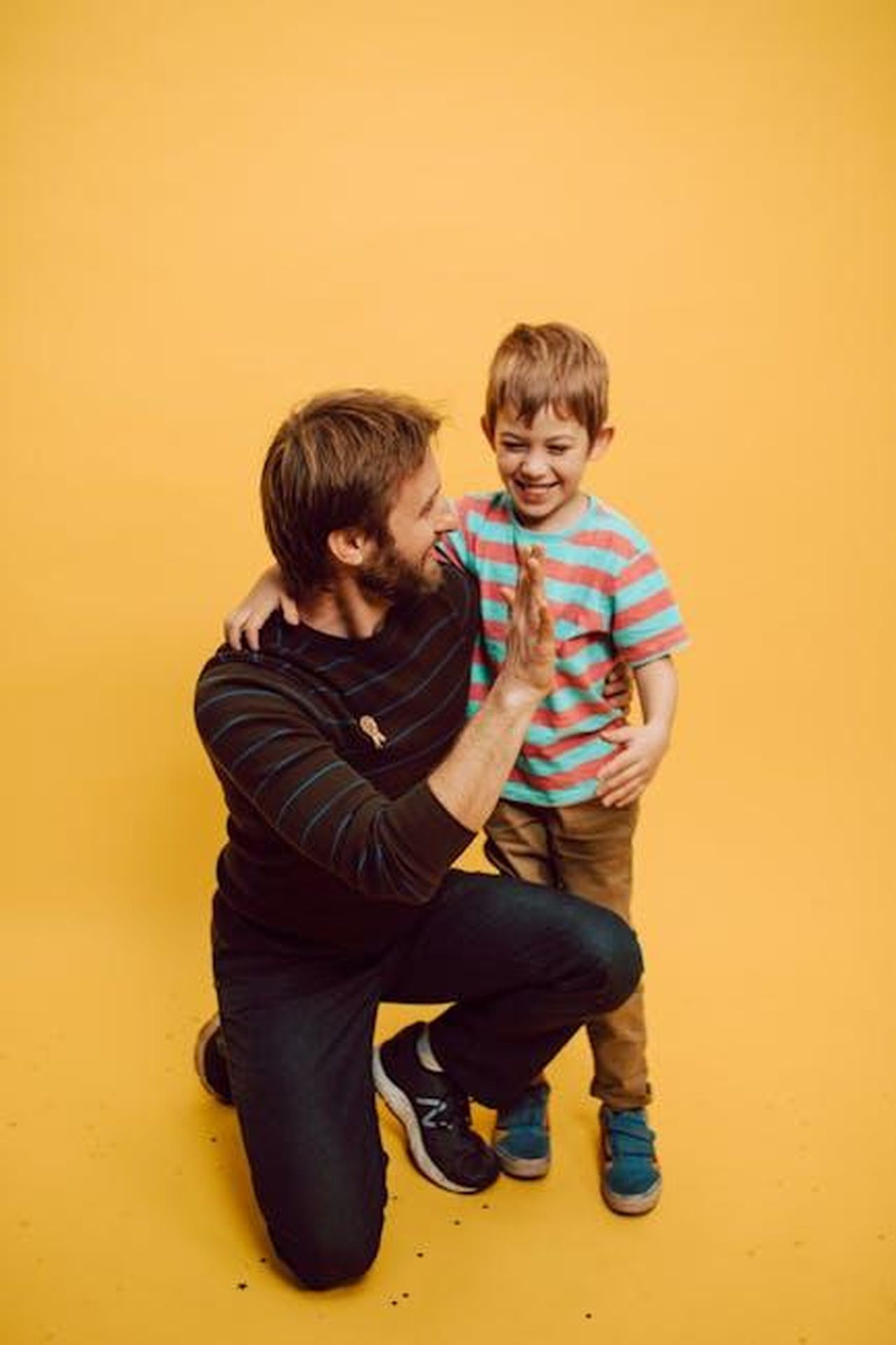 Father_Knows_Best_19541960_35mgTpTvY2 - Confidenze24 Source: RDNE Stock project - pexels - Father and son sharing a joyful high five indoors against a vibrant yellow background.