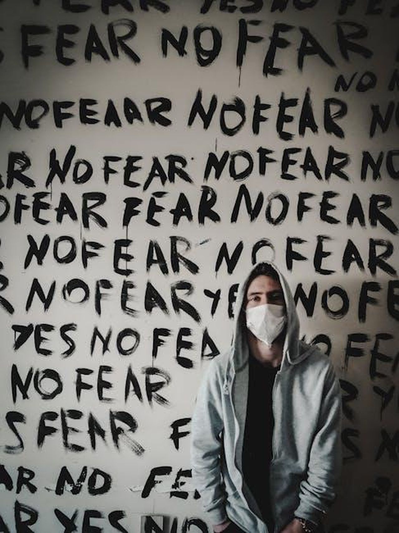 Frank_parla_della_sua_malattia_QR7jaqikhm - Confidenze24 Source: Korhan Erdol - pexels - Person in a hoodie with mask stands before 'No Fear' graffiti wall, emphasizing bold expression.