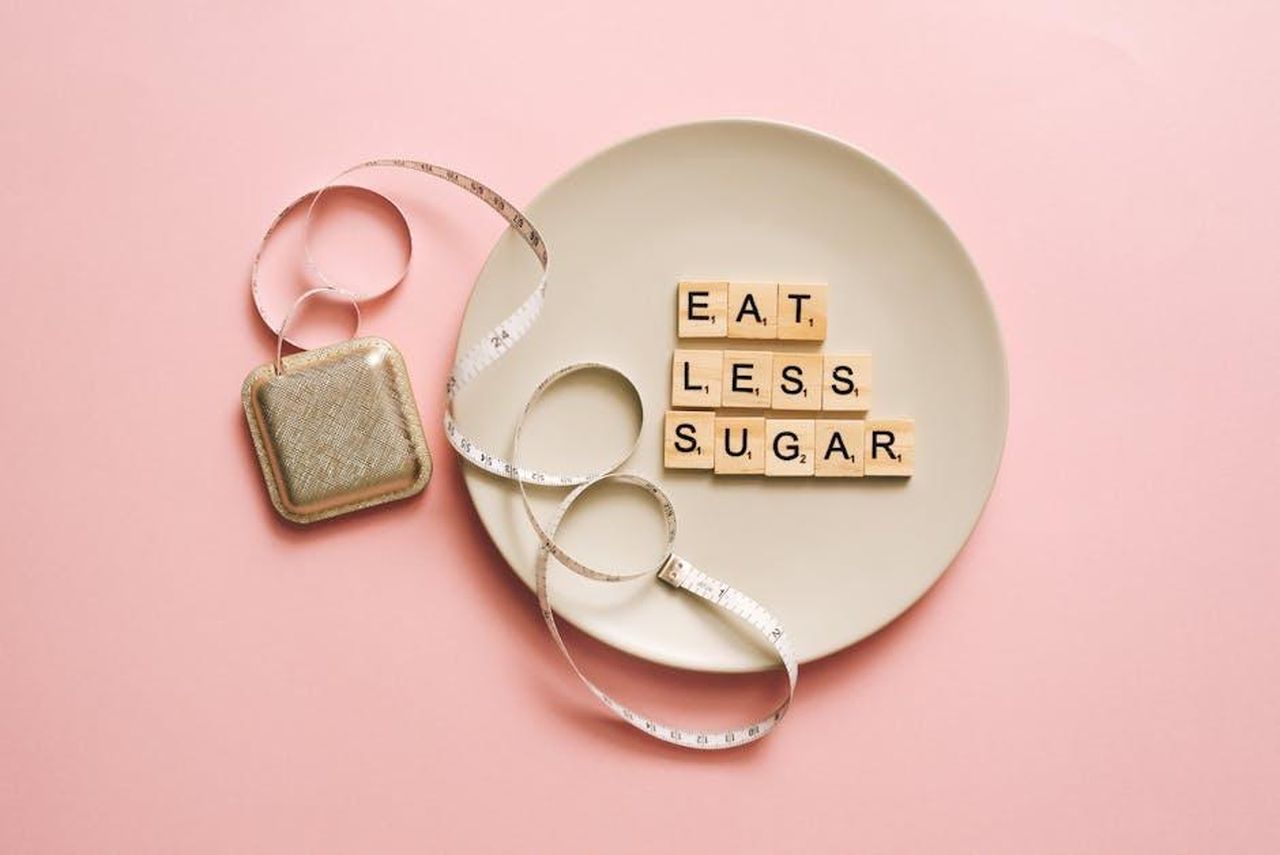 Gemma_Collins_su_quanto_peso_intende_perdere_f6geH3LGE6 - Confidenze24 Source: Leeloo The First - pexels - Flat lay of Scrabble tiles saying 'Eat Less Sugar' on a plate with a tape measure on a pink background.