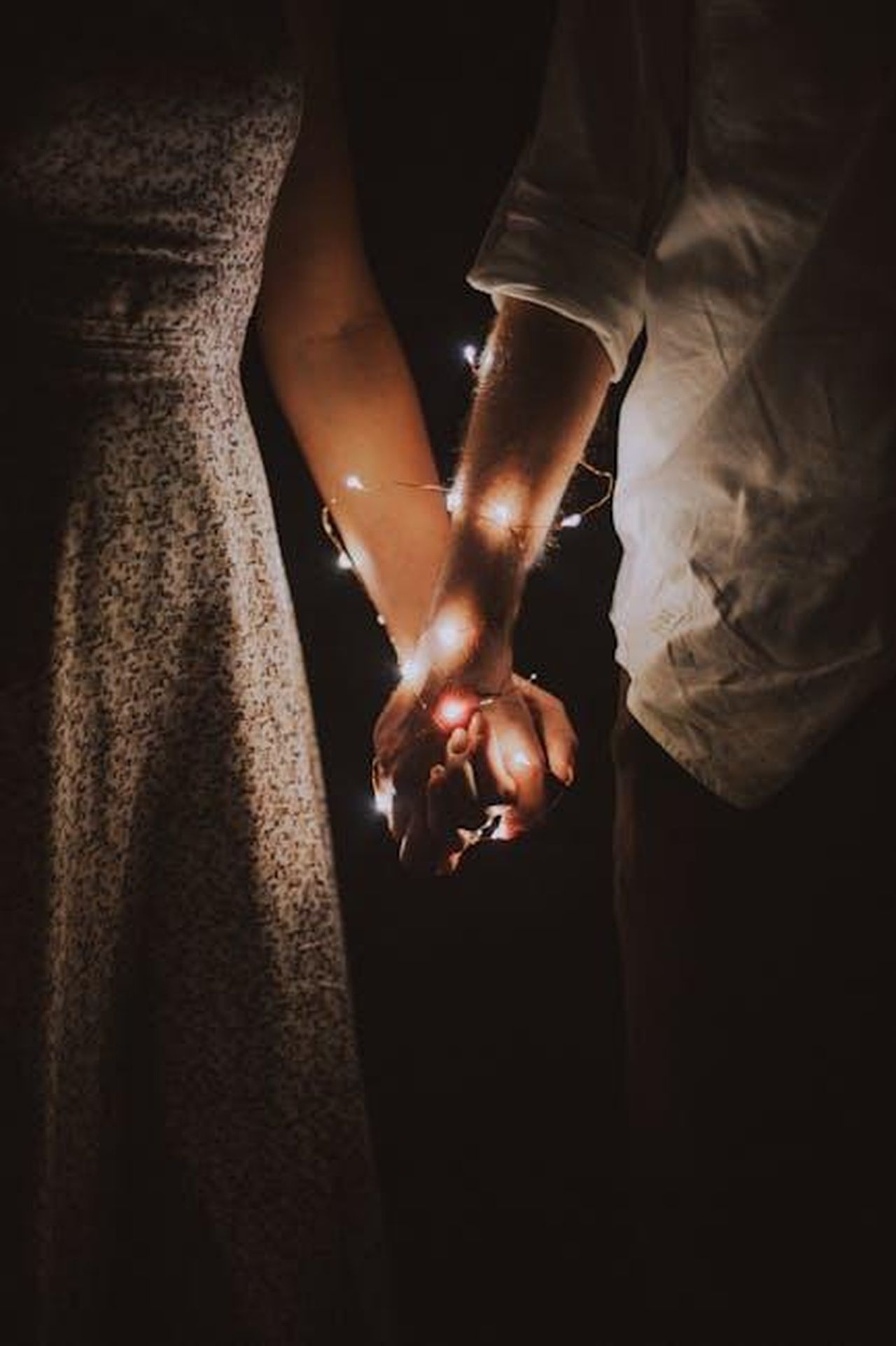 Georgia_Toffolo_e_James_amAZDAwD6x - Confidenze24 Source: Anastasiya Lobanovskaya - pexels - A warm and intimate close-up of a couple holding hands adorned with glowing string lights.