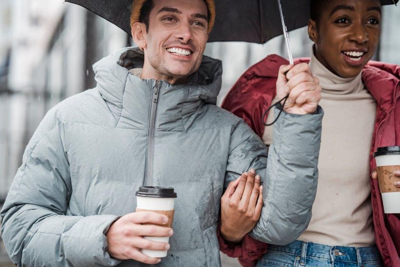 Giacca_puffer_cropped_in_down_responsabile_XvrnreP8SG - Confidenze24 Source: Klaus Nielsen - pexels - Smiling couple walking outdoors under umbrella while enjoying coffee on a rainy day.